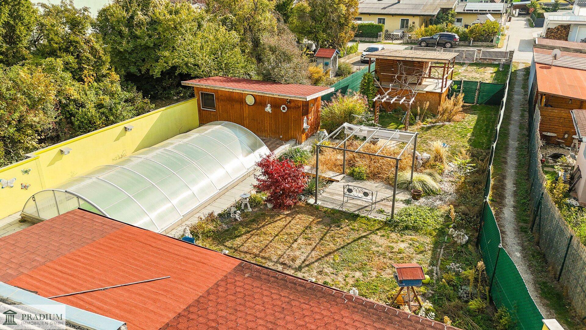 Vogelperspektive des Gartens mit Pool, Gartenhaus und weiteren Nebengebäuden, umgeben von Grünflächen.