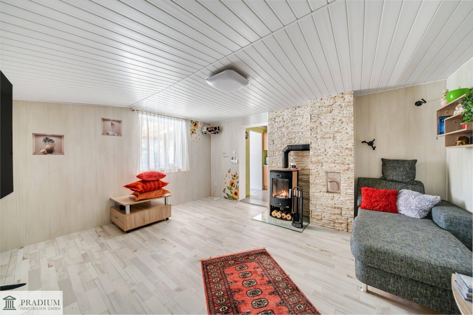 Gemütliches Wohnzimmer mit Holzofen, Steinwandakzent und hellem Laminatboden, eingerichtet mit Sofa und Teppich.