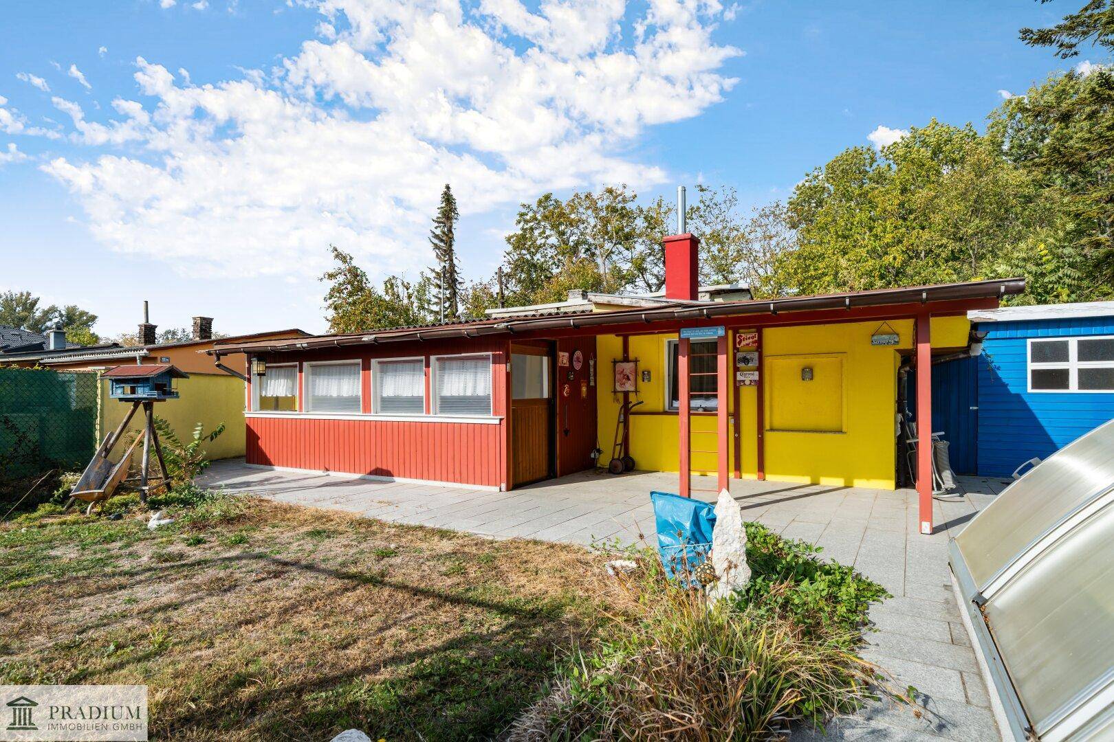Buntes Haus mit roter und gelber Fassade, davor eine gepflasterte Terrasse und ein kleiner Gartenbereich.