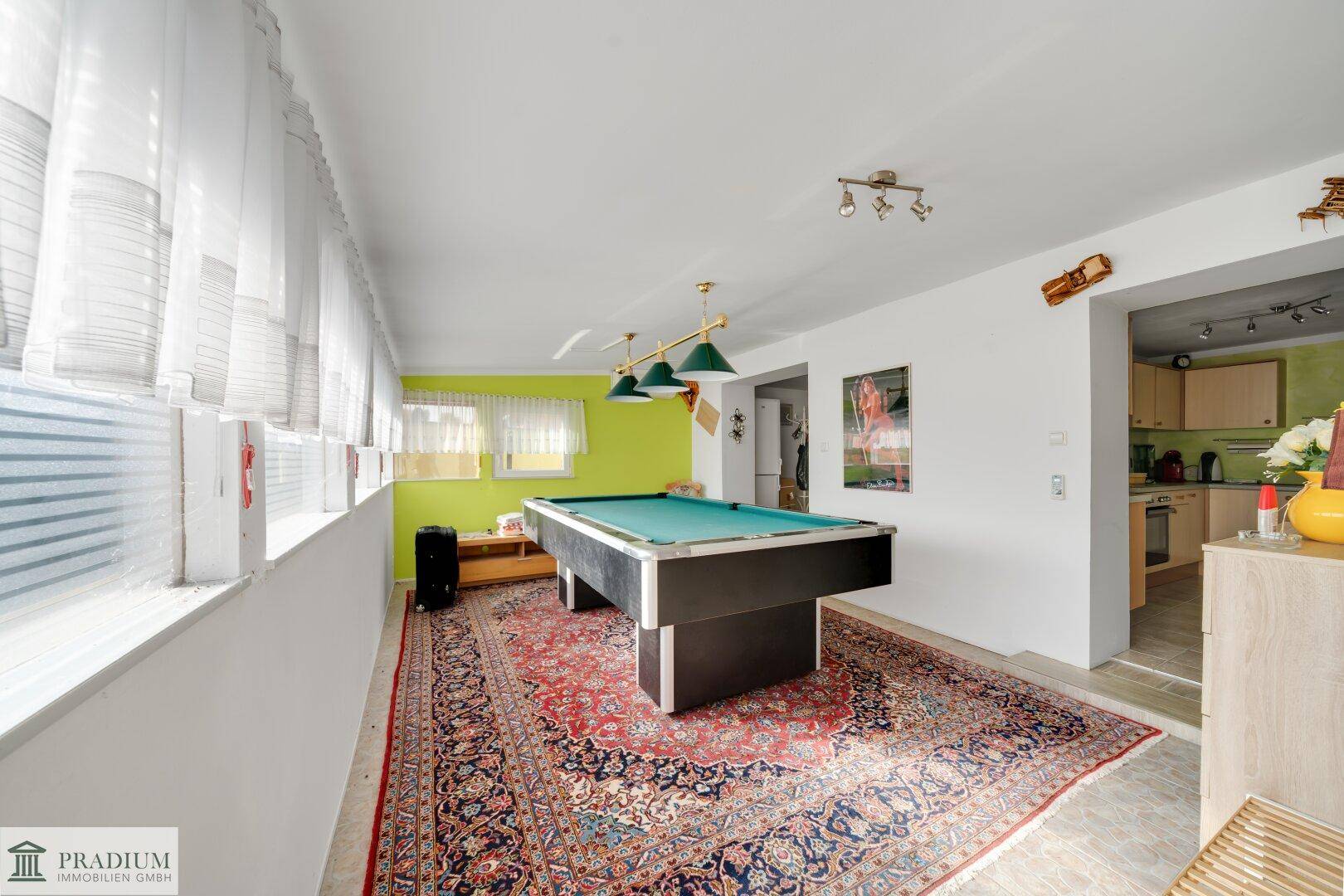 Geräumiger Spielraum mit Billardtisch und großem Teppich, angrenzend an eine Küche, mit hellgrüner Akzentwand.