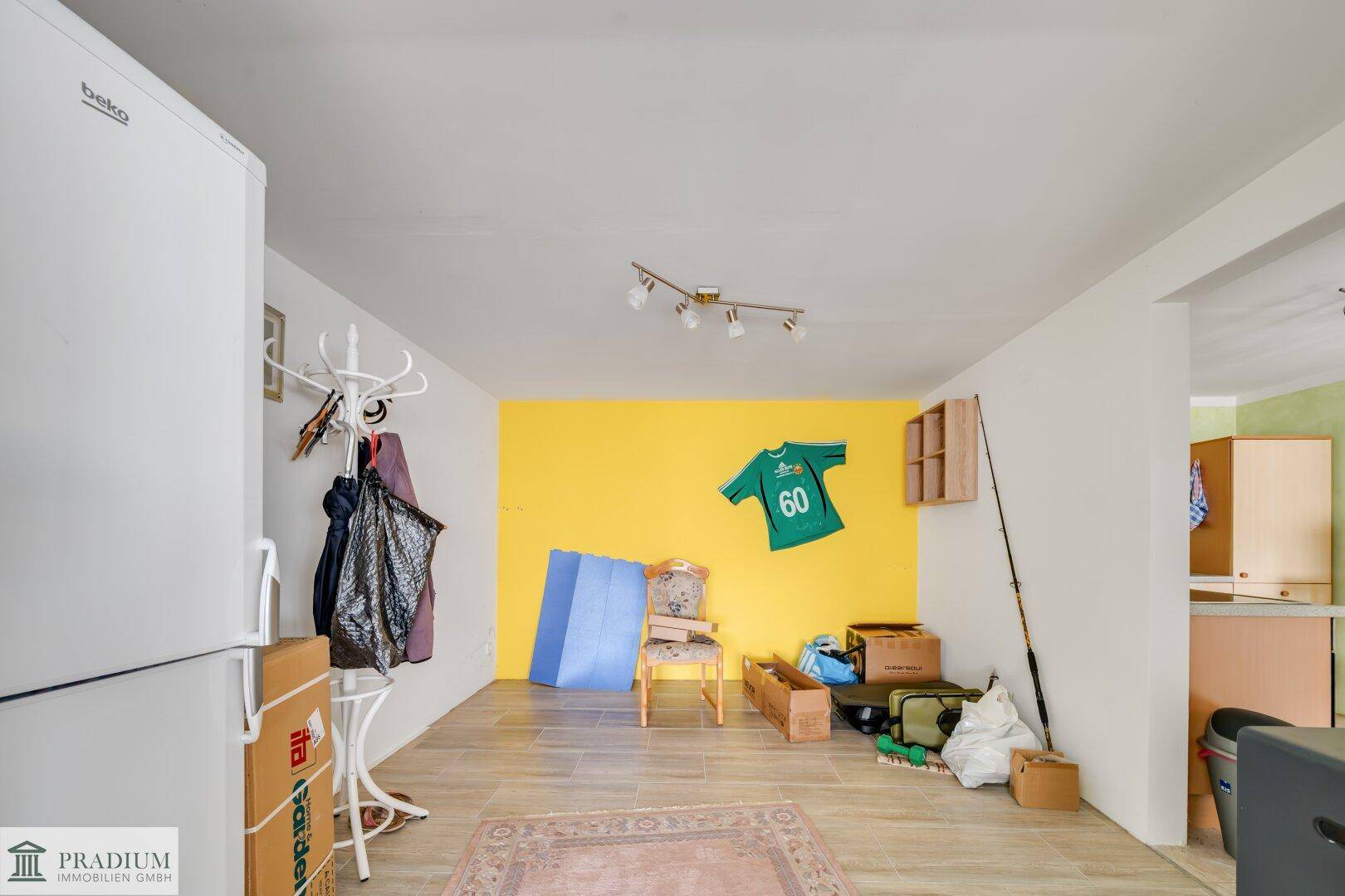 Heller Flurbereich mit gelber Akzentwand und Stauraum, angrenzend an die Küche, mit Kühlschrank und Garderobe.