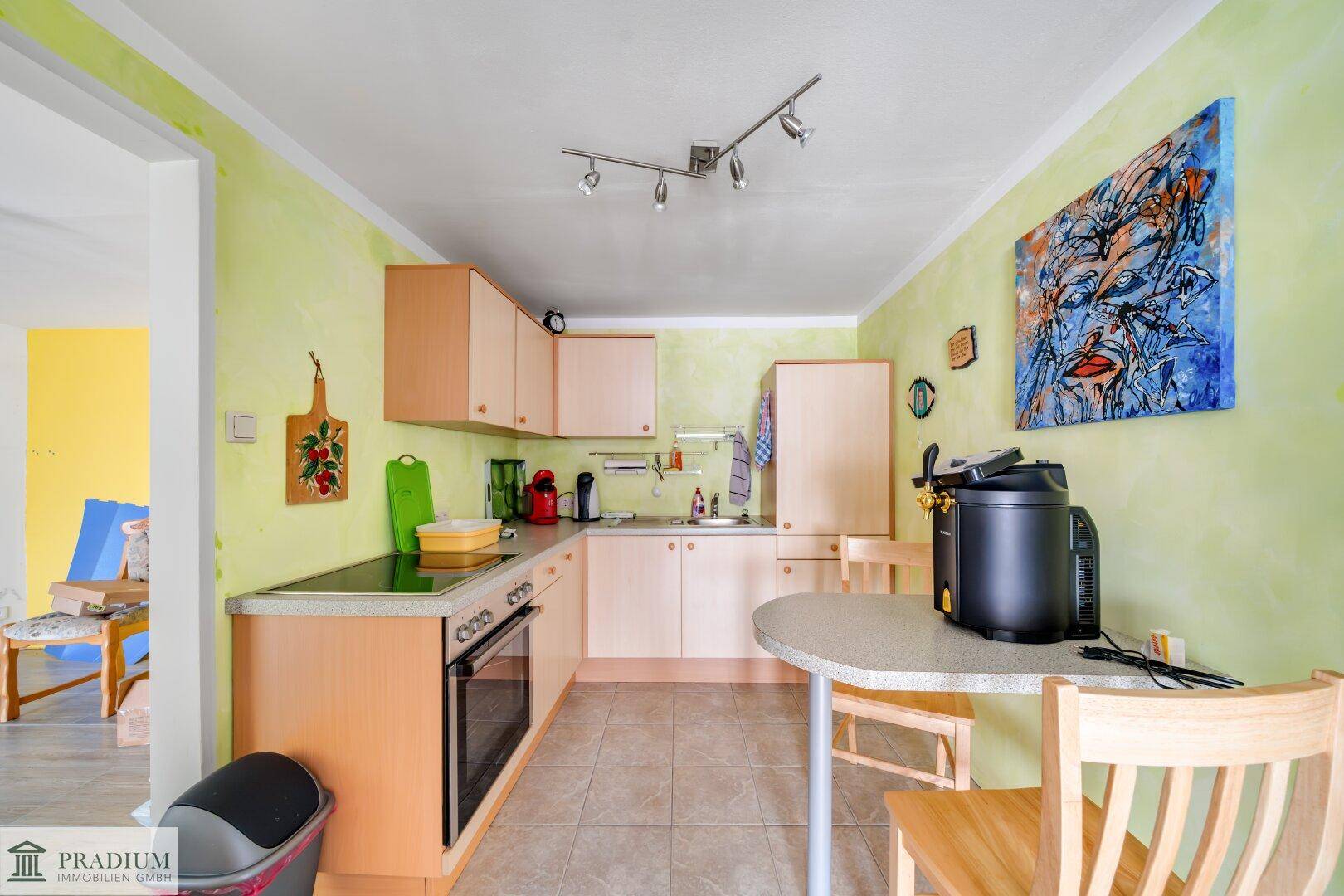 Funktionale Küche mit hellen Holzschränken, Essbereich und Fliesenboden, beleuchtet von einer Deckenleuchte.