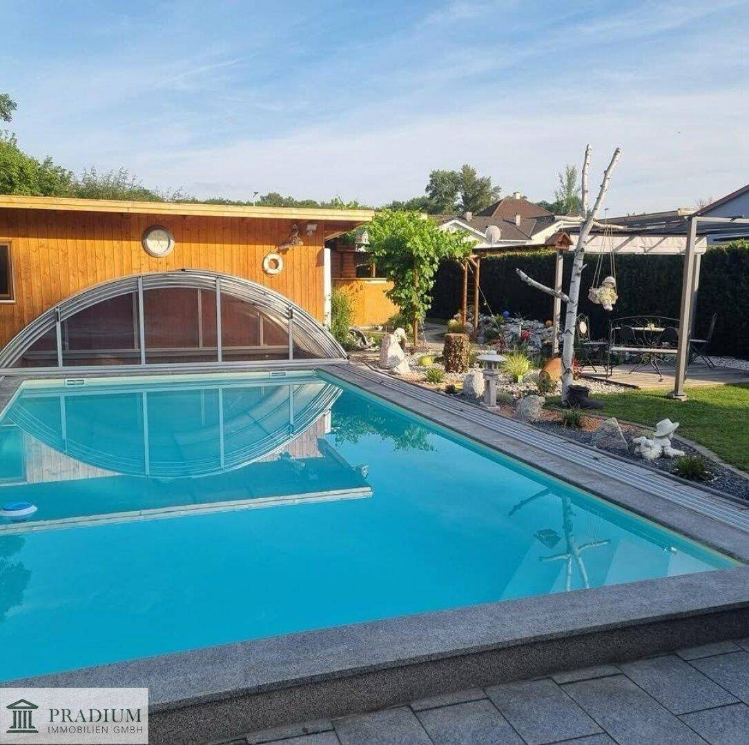 Außenbereich mit großem Swimmingpool, umgeben von einer Holzterrasse und gepflegtem Garten mit Pflanzen.