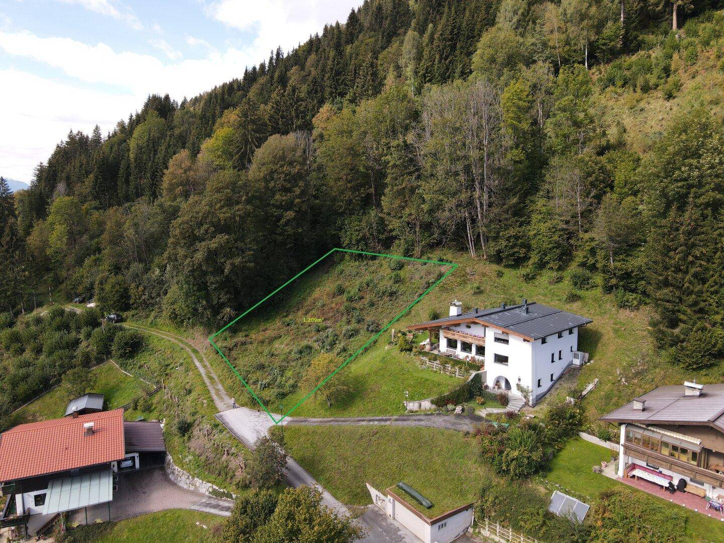 Luftaufnahme eines umgrenzten Grundstücks neben einem Haus in einer bewaldeten Berglandschaft.