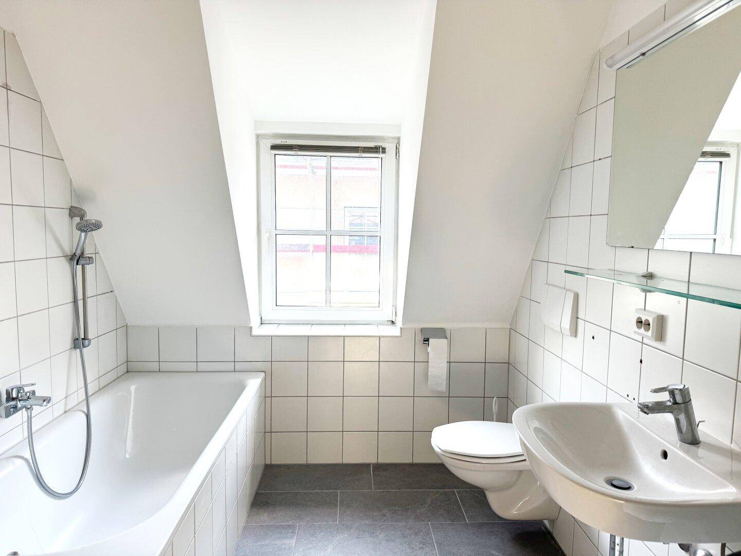 Helles Badezimmer mit Badewanne, Waschbecken, WC und Dachschräge.