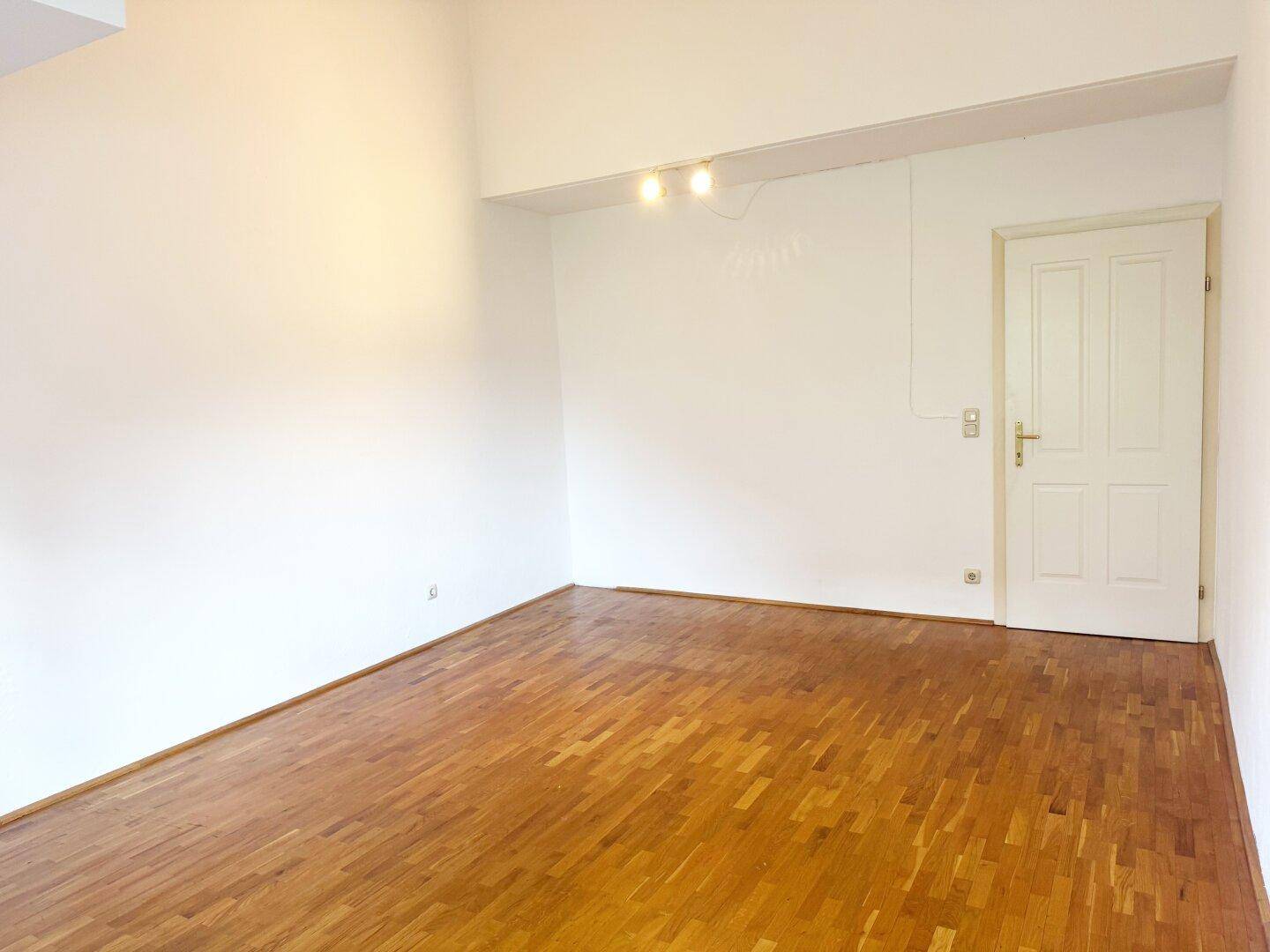 Heller, leerer Raum mit Parkettboden und einer weißen Tür.