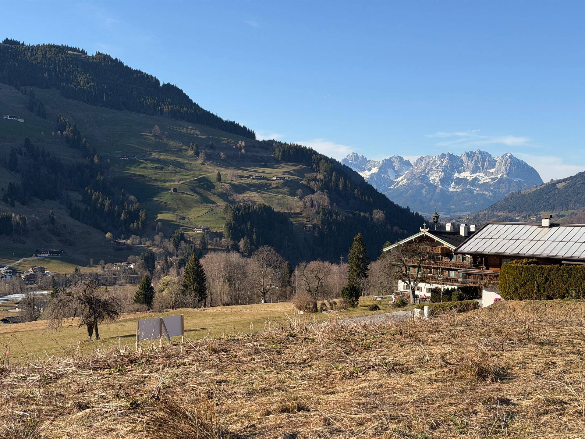 Weitläufige grüne Landschaft mit einem traditionellen Haus und schneebedeckten Bergen im Hintergrund.