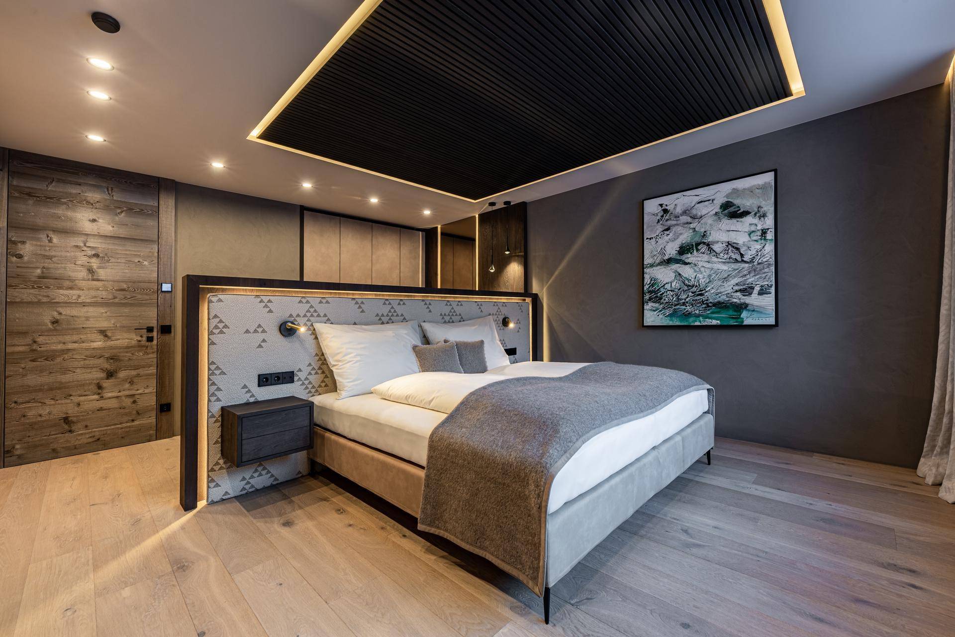 Stilvolles Schlafzimmer mit großem Bett, Holzboden und moderner Kunst an der Wand, gut beleuchtet.