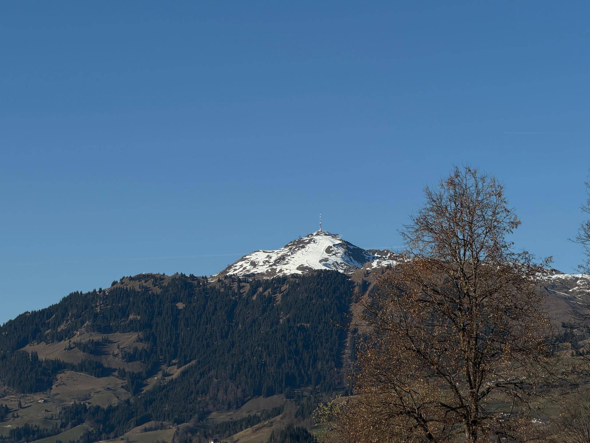 Klare Sicht auf einen schneebedeckten Berggipfel mit einem Sendemast unter strahlend blauem Himmel.