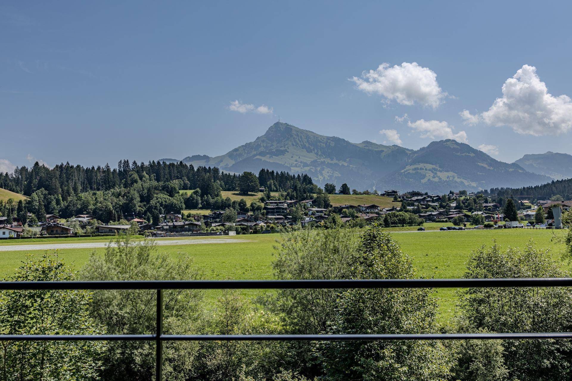 Weitblick von einem Balkon über eine grüne Landschaft mit einem Dorf und Bergen im Hintergrund.
