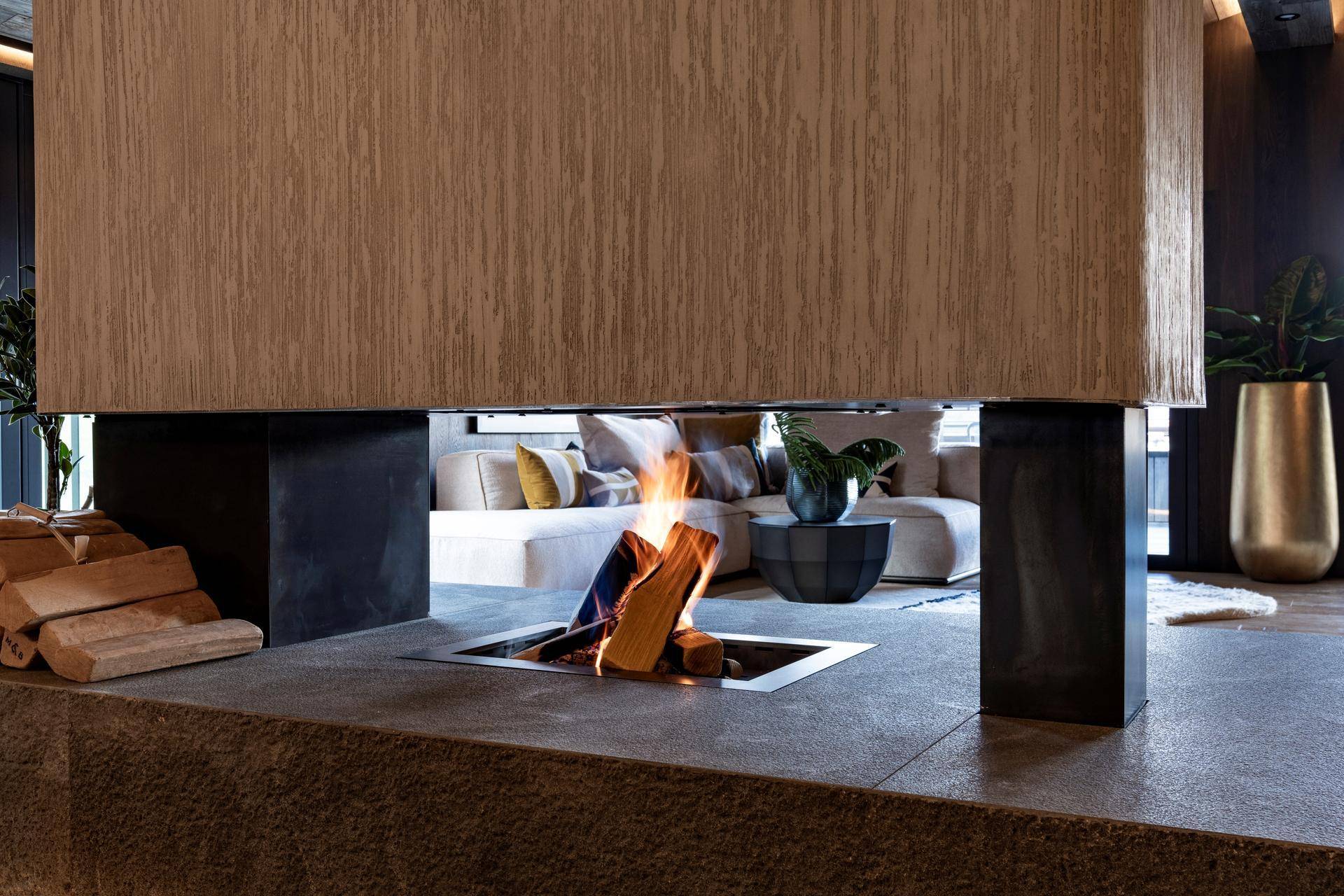 Detailaufnahme eines modernen Kamins mit brennendem Holz und rustikalem Steinsockel im Wohnbereich.