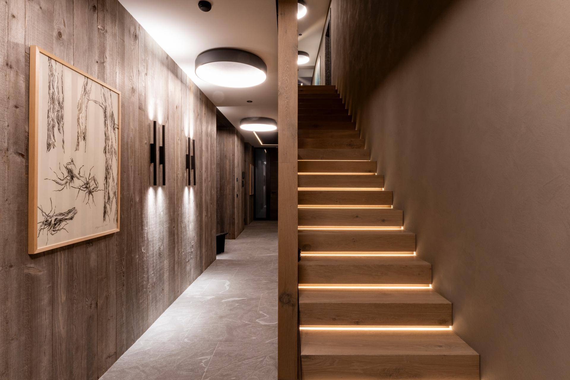 Heller Flur mit Holzverkleidung, beleuchteter Treppe und moderner Wandkunst.