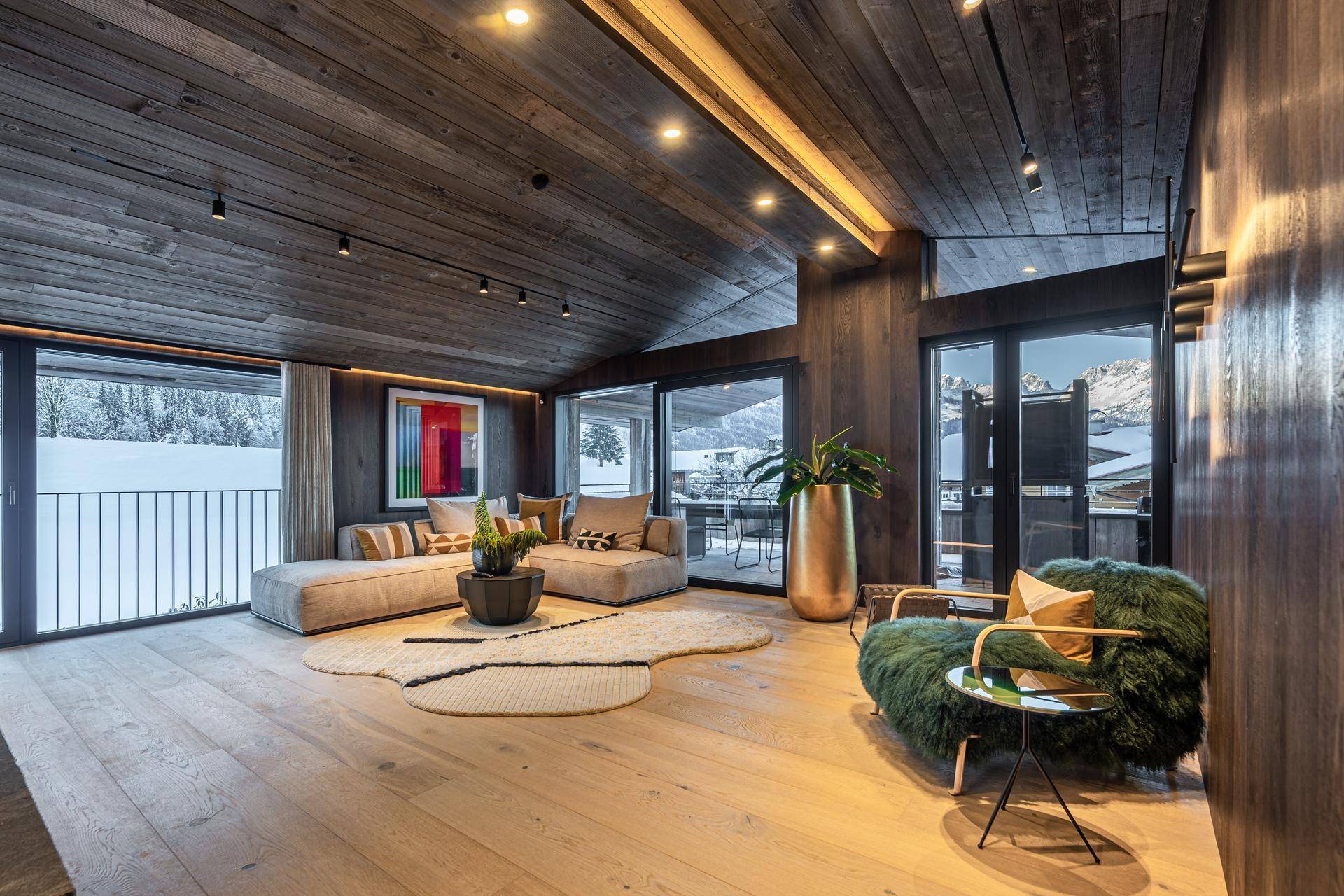 Großzügiges Wohnzimmer mit Holzboden, bequemen Sofas und Blick auf die verschneite Landschaft durch große Fenster.