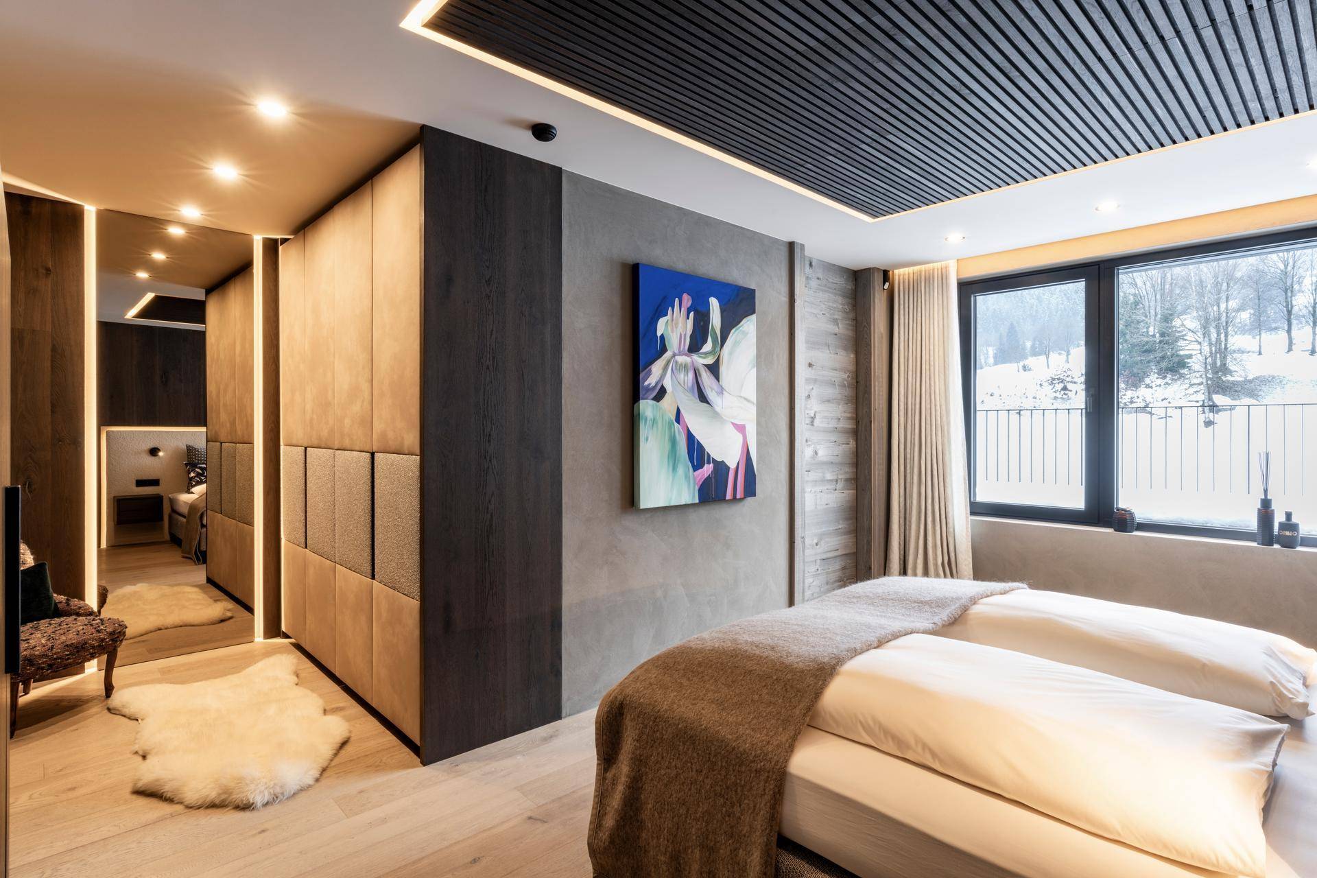 Modernes Schlafzimmer mit Holzboden, Kunstwerk und Blick auf die verschneite Landschaft.