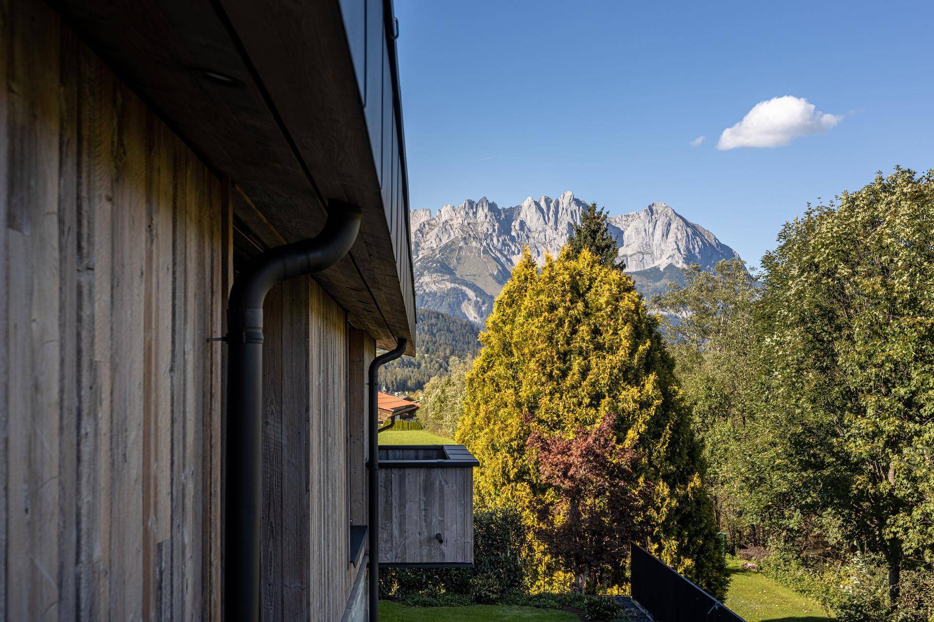 Holzfassade des Gebäudes mit Blick auf majestätische Berge und üppige, herbstliche Vegetation.