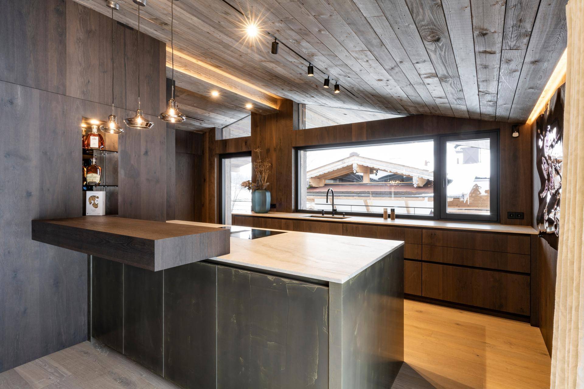 Moderne Holzküche mit Kücheninsel, integrierten Geräten und großem Fenster mit Ausblick auf die Winterlandschaft.