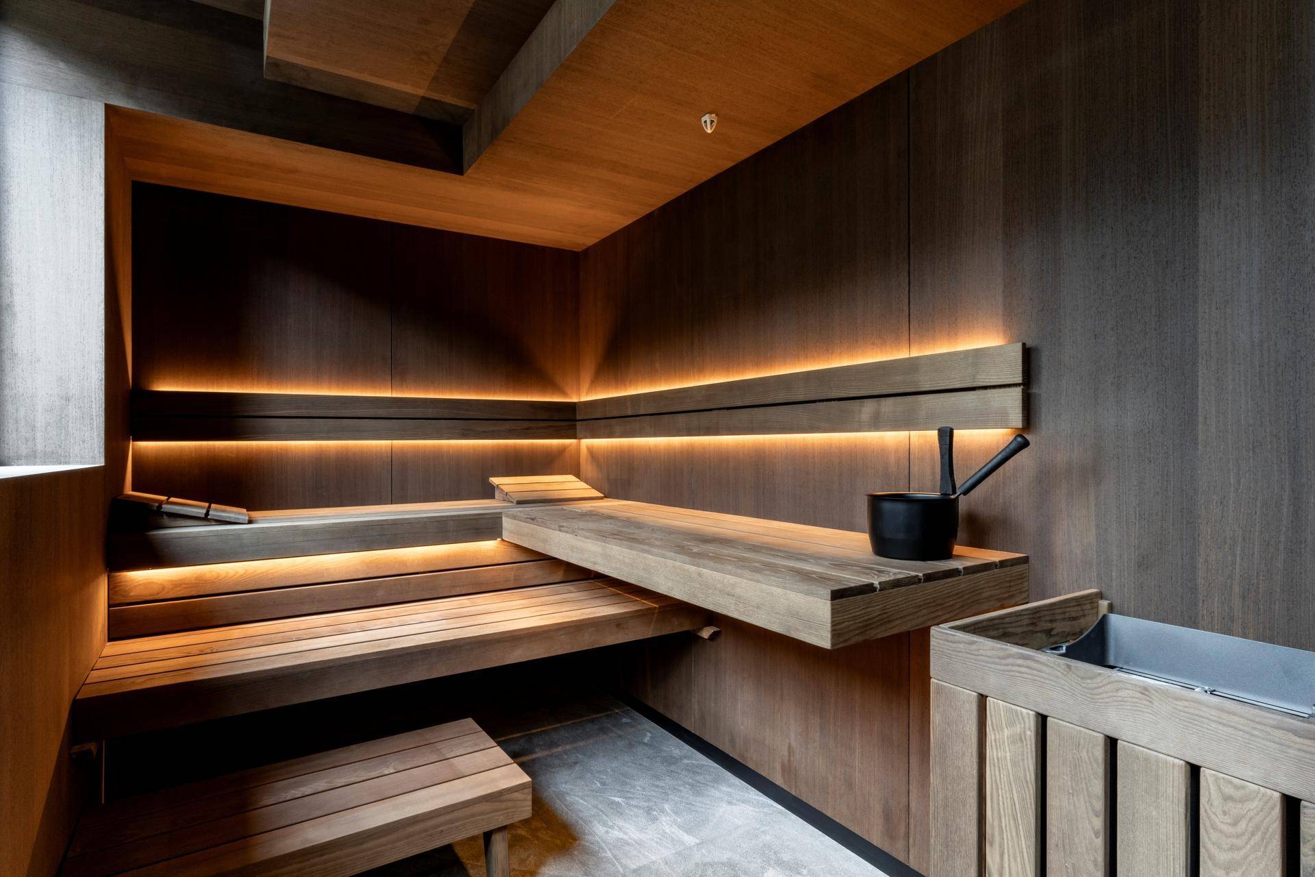 Elegante Sauna mit dunkler Holzverkleidung, breiten Bänken und indirekter Beleuchtung für Entspannung.