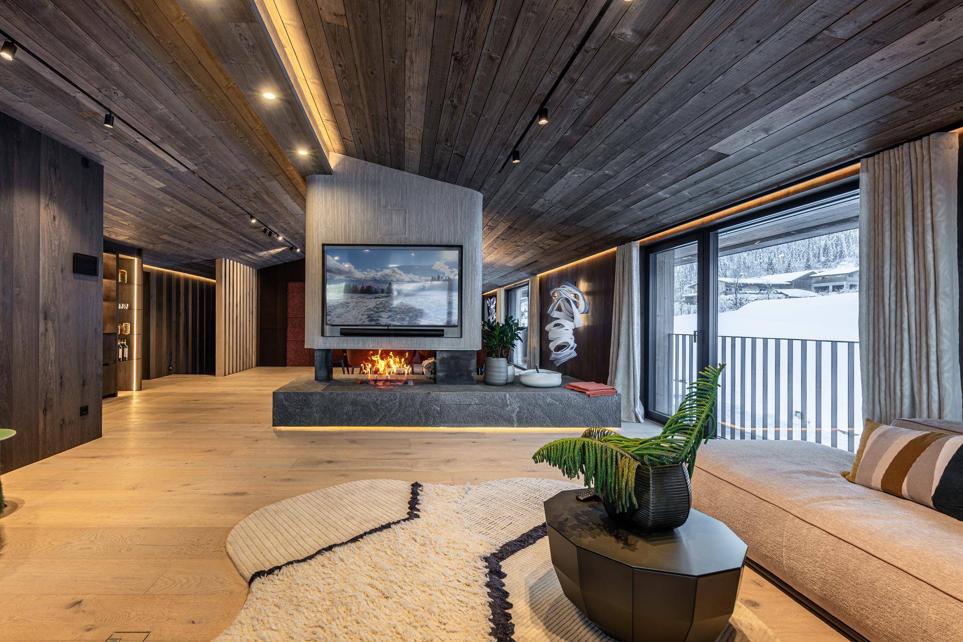 Stilvolles Wohnzimmer mit modernem Kamin, Holzboden und Zugang zu einem Balkon mit Winterlandschaft.