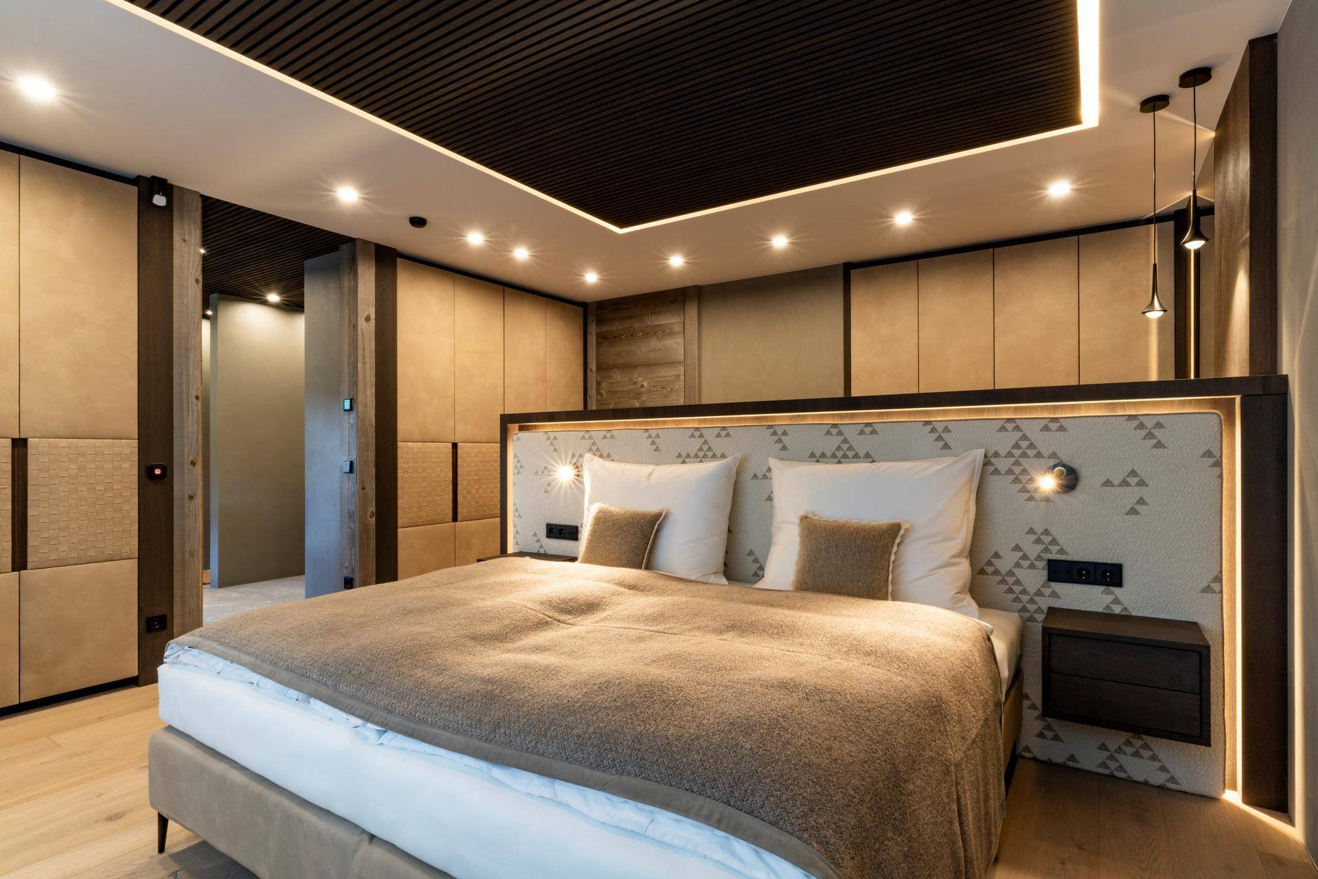 Komfortables Schlafzimmer mit großem Doppelbett, Holzboden und eleganten Einbauschränken in warmen Farbtönen.