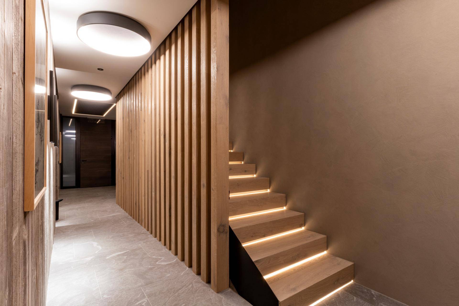 Moderner Flur mit Holzlamellenwand, beleuchteter Treppe und Fliesenboden für ein stilvolles Ambiente.
