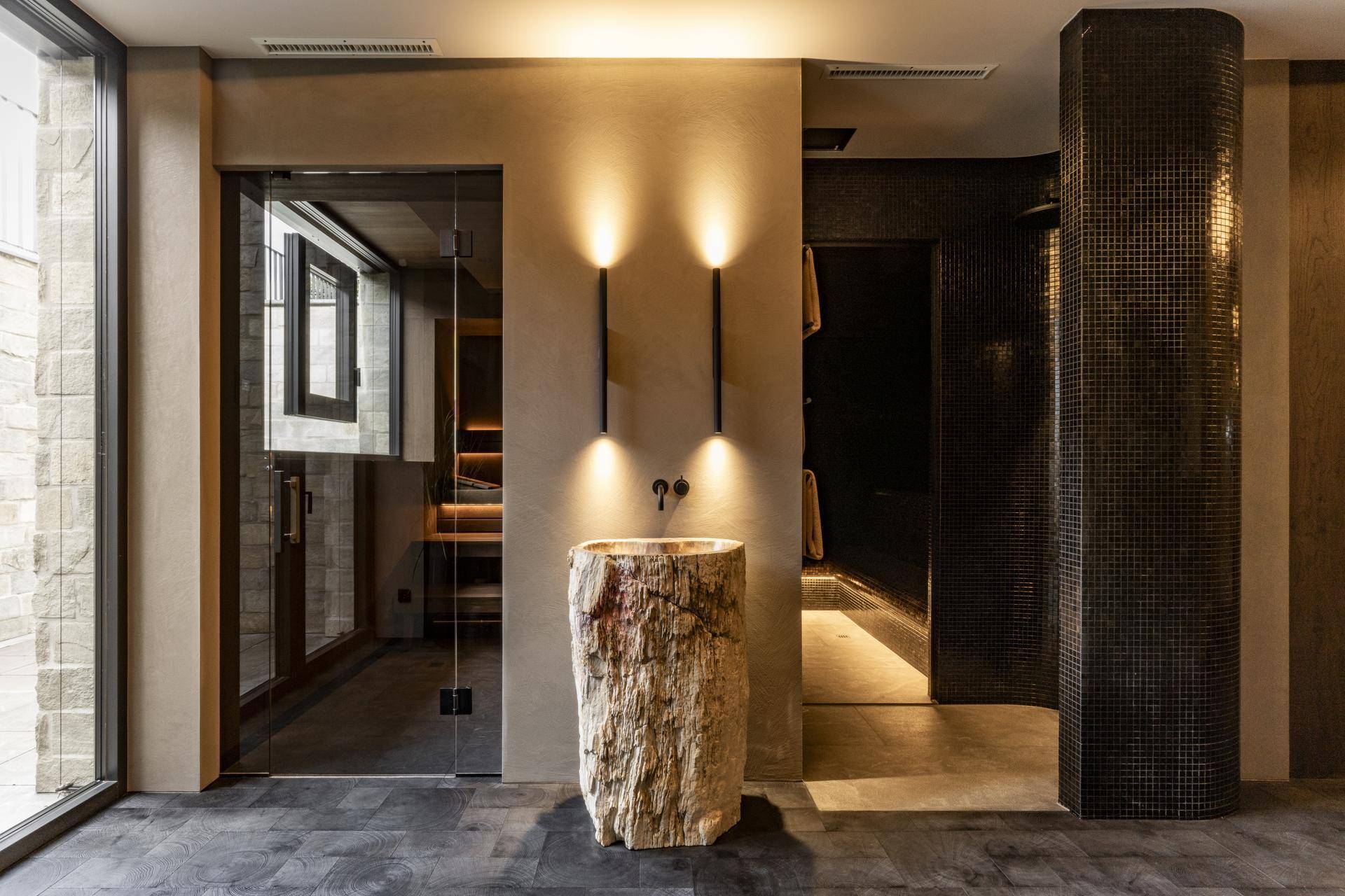 Eingangsbereich zum Wellnessbereich mit Natursteinwaschbecken und Glaswand zur Sauna.