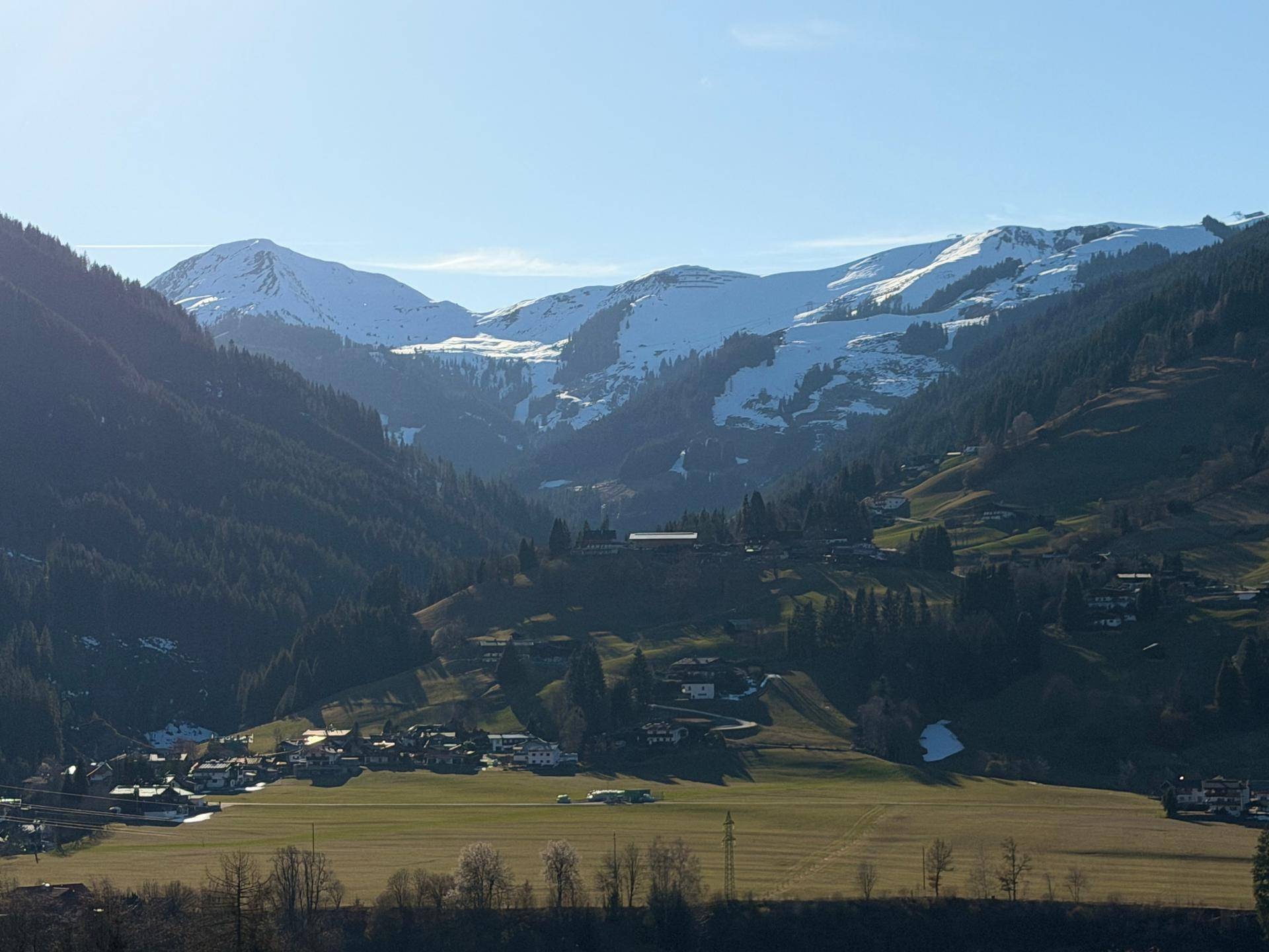 Weitläufiges Tal mit kleinen Siedlungen, umgeben von bewaldeten Bergen und schneebedeckten Gipfeln.
