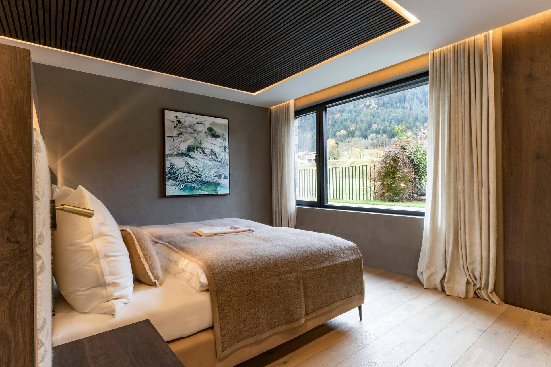 Helles Schlafzimmer mit Holzboden, großem Fenster und Blick auf die grüne Natur.