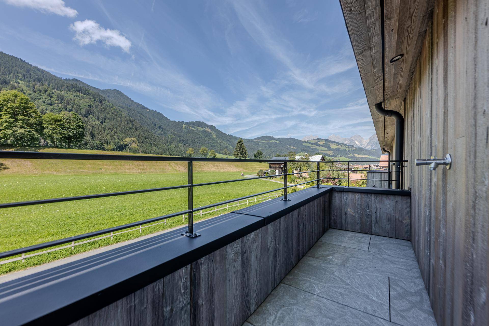 Kleiner Balkon mit modernem Metallgeländer und idyllischem Blick auf grüne Wiesen und Berge.