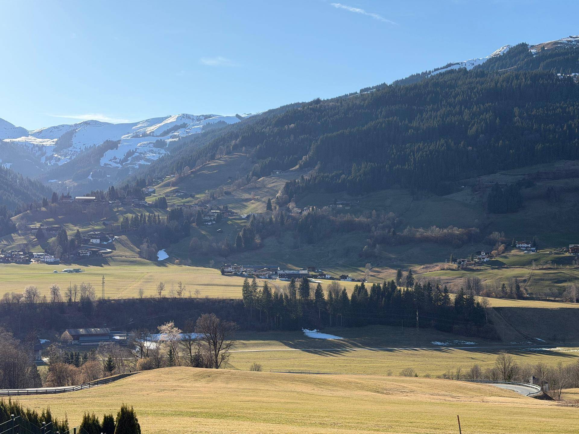 Malerische Hügellandschaft mit grünen Wiesen, Wäldern und vereinzelten Häusern in der Ferne.