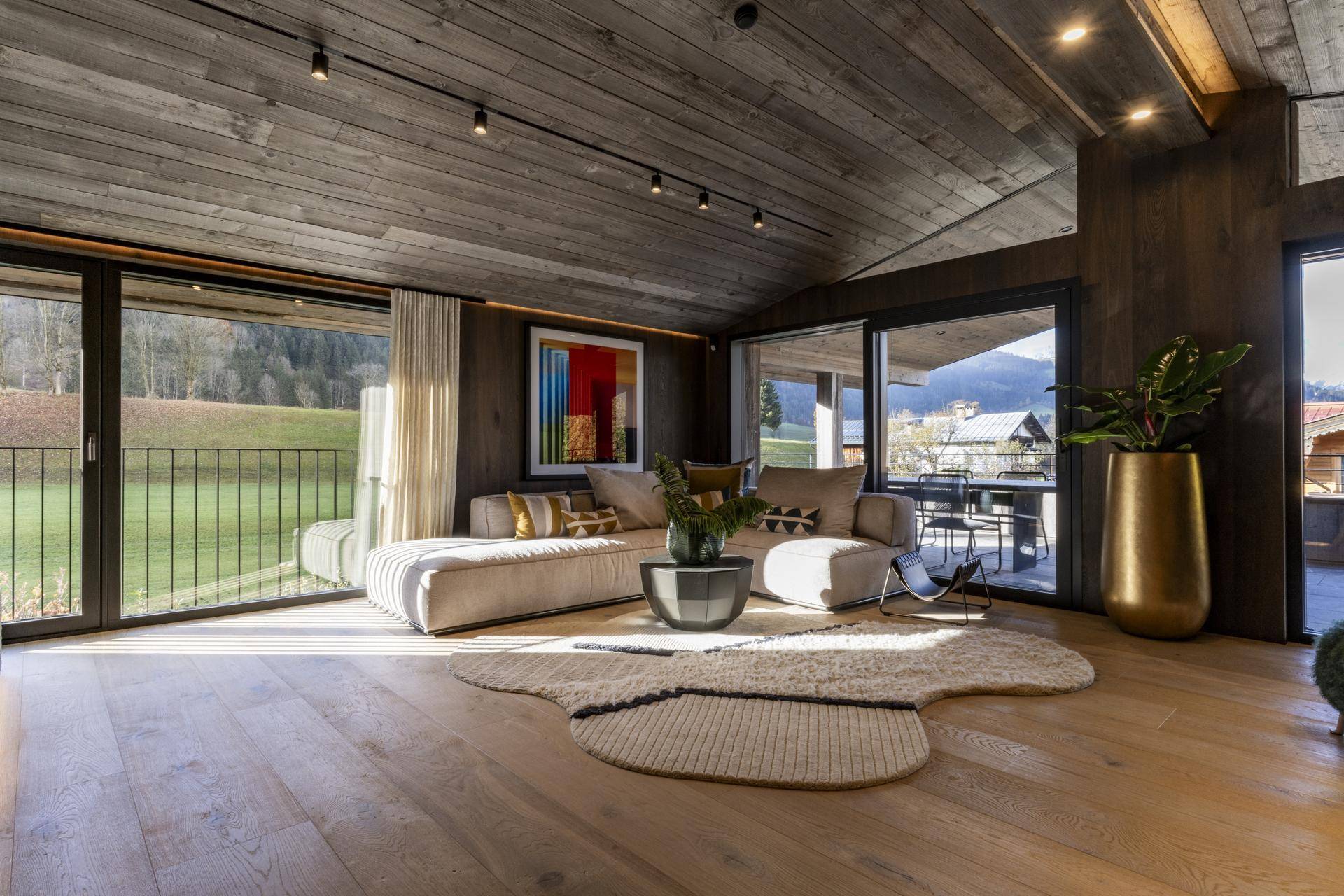 Geräumiges Wohnzimmer mit Holzboden, großen Fenstern und Blick auf die grüne Landschaft.