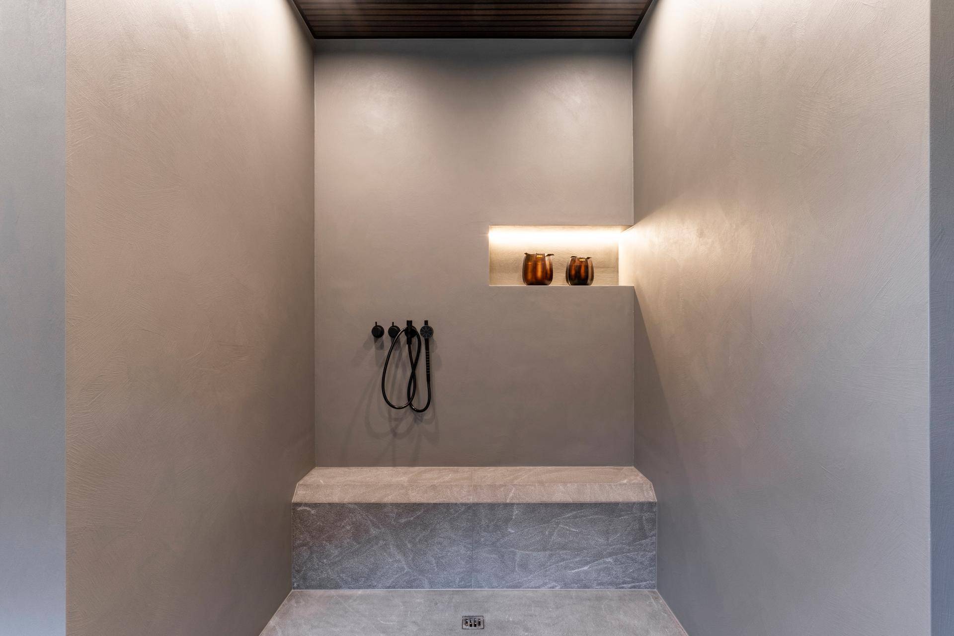 Moderne Duschkabine mit minimalistischem Design, Steinbank und indirekter Beleuchtung.
