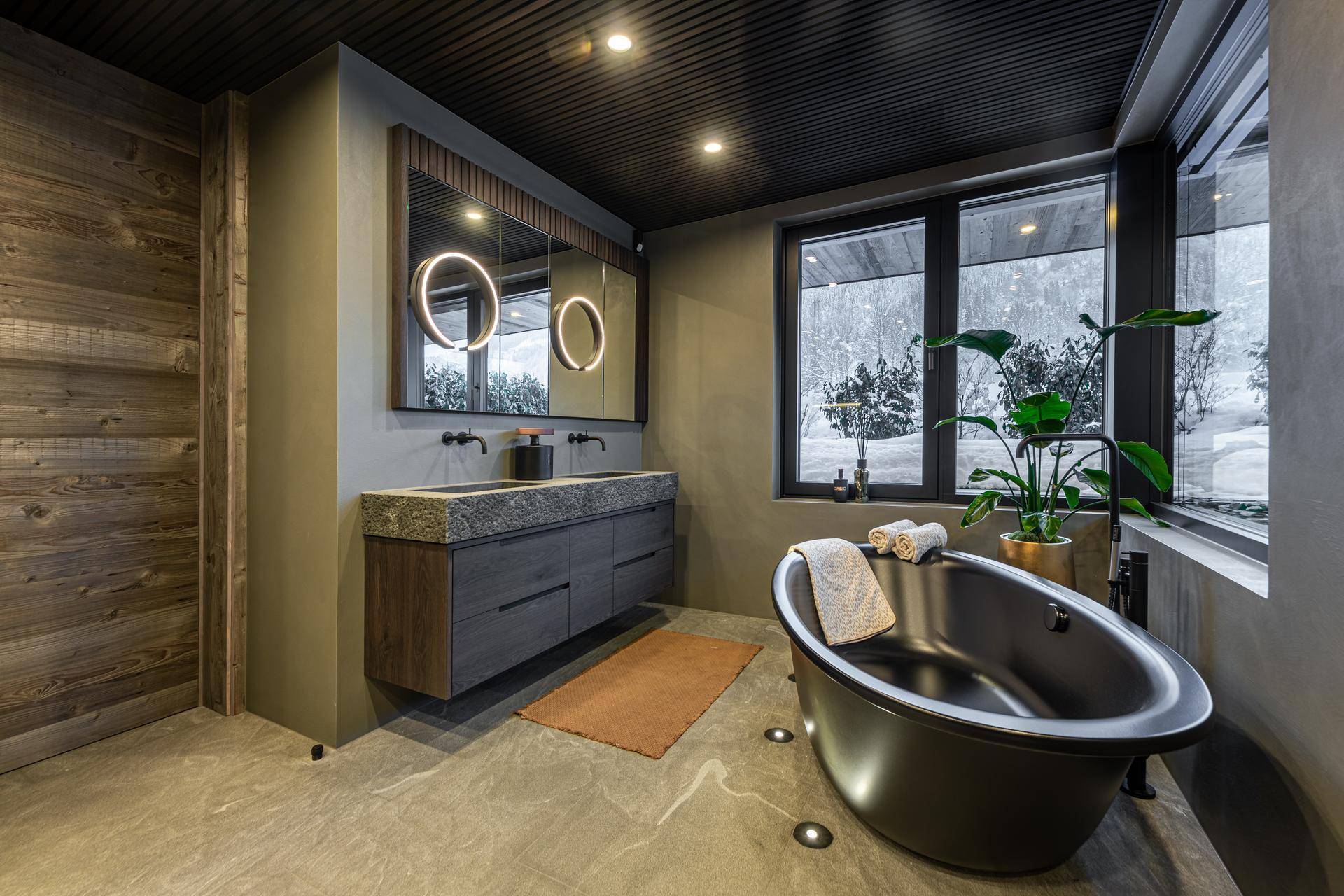 Luxuriöses Badezimmer mit freistehender Badewanne, Doppelwaschbecken und großem Fenster mit Winterblick.