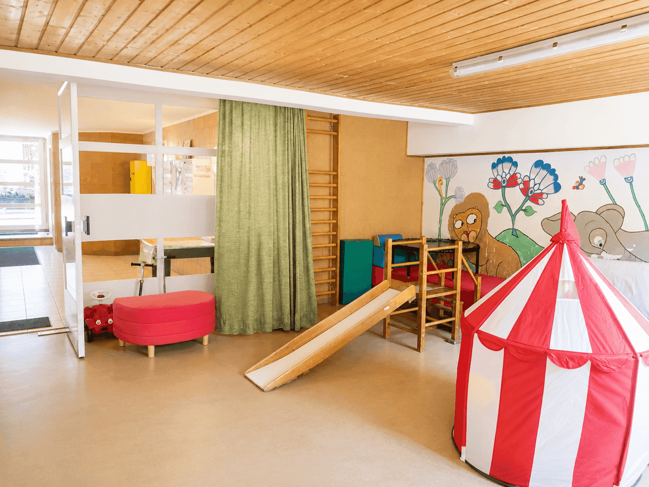 Großer Raum mit Spielgeräten, Holzwänden und farbenfroher Wandmalerei.