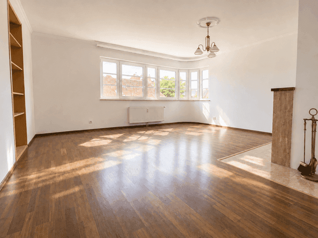 Großes, leeres Wohnzimmer mit Holzboden, Erkerfenstern und Kamin.