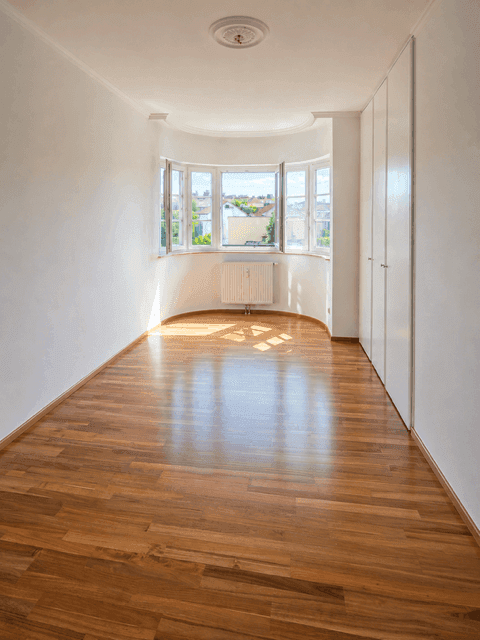 Leeres Zimmer mit Holzboden, Erkerfenstern und Einbauschränken, ideal als Schlafzimmer.