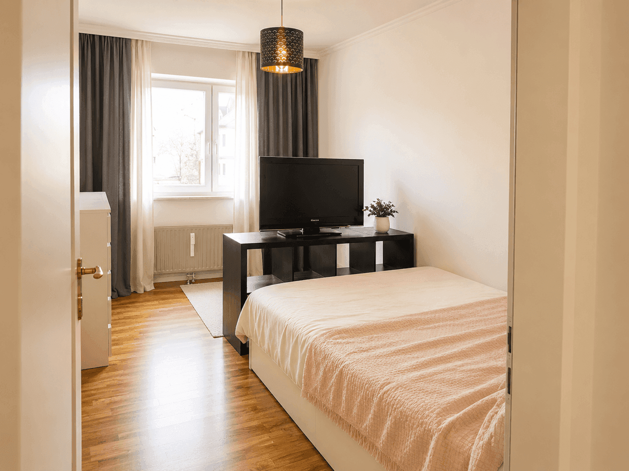 Schlafzimmer mit Holzboden, Fenster, Fernseher und einem Bett mit Stauraum.