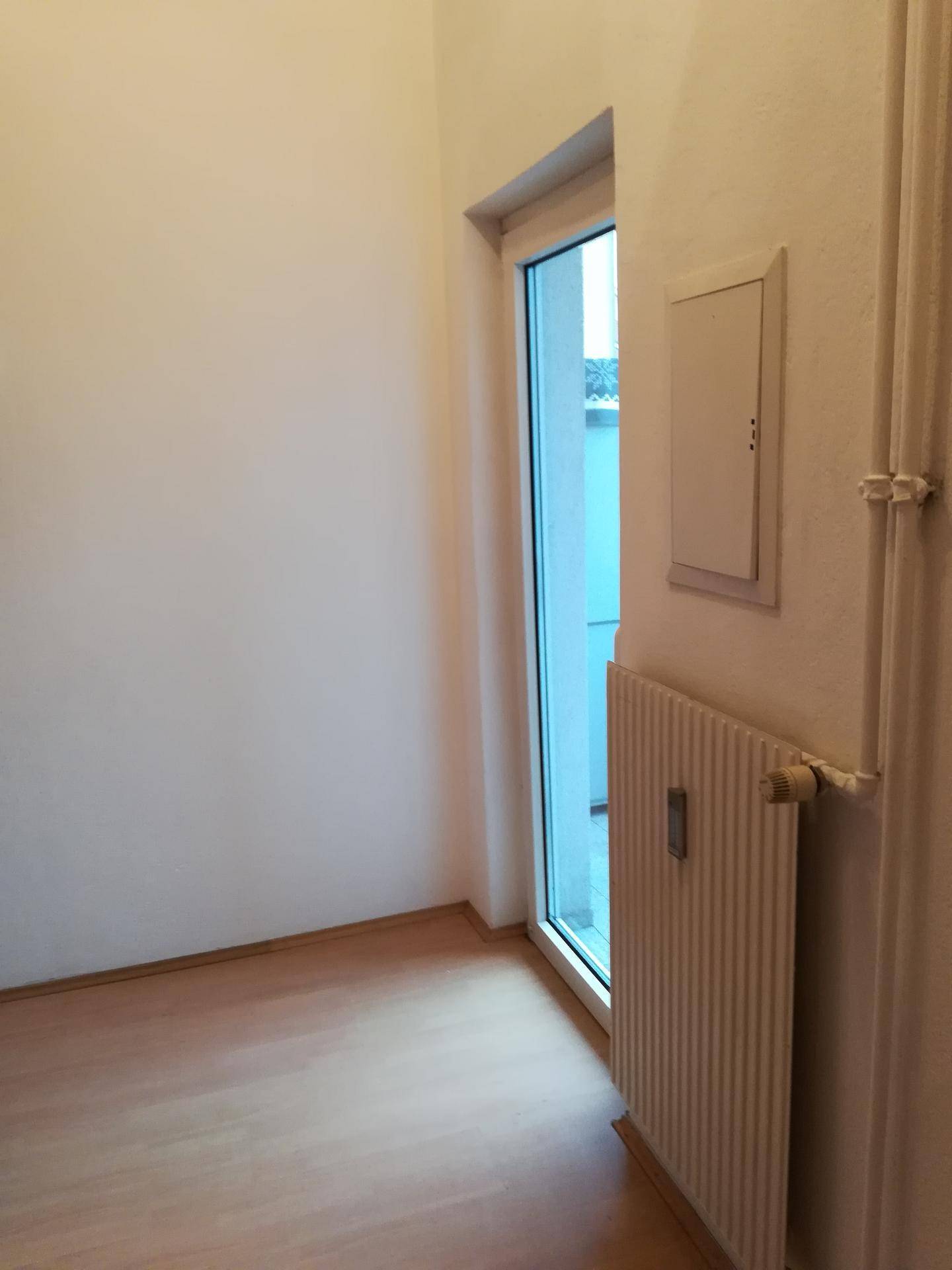 Heller Raum mit Laminatboden, großem Fenster und Heizkörper, der viel natürliches Licht hereinlässt.