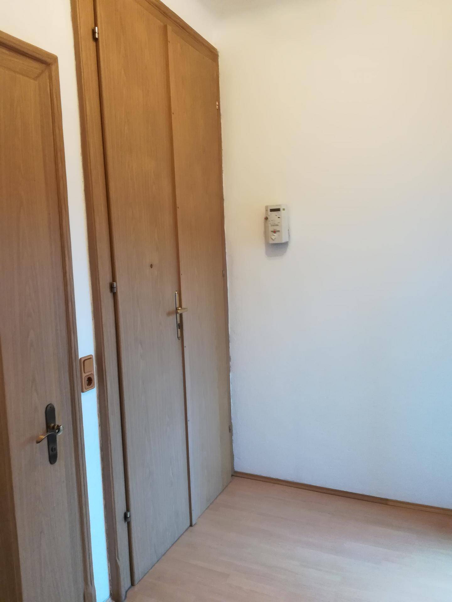 Leerer Raum mit hellem Laminatboden und integrierten Holzschränken, der vielseitig genutzt werden kann.