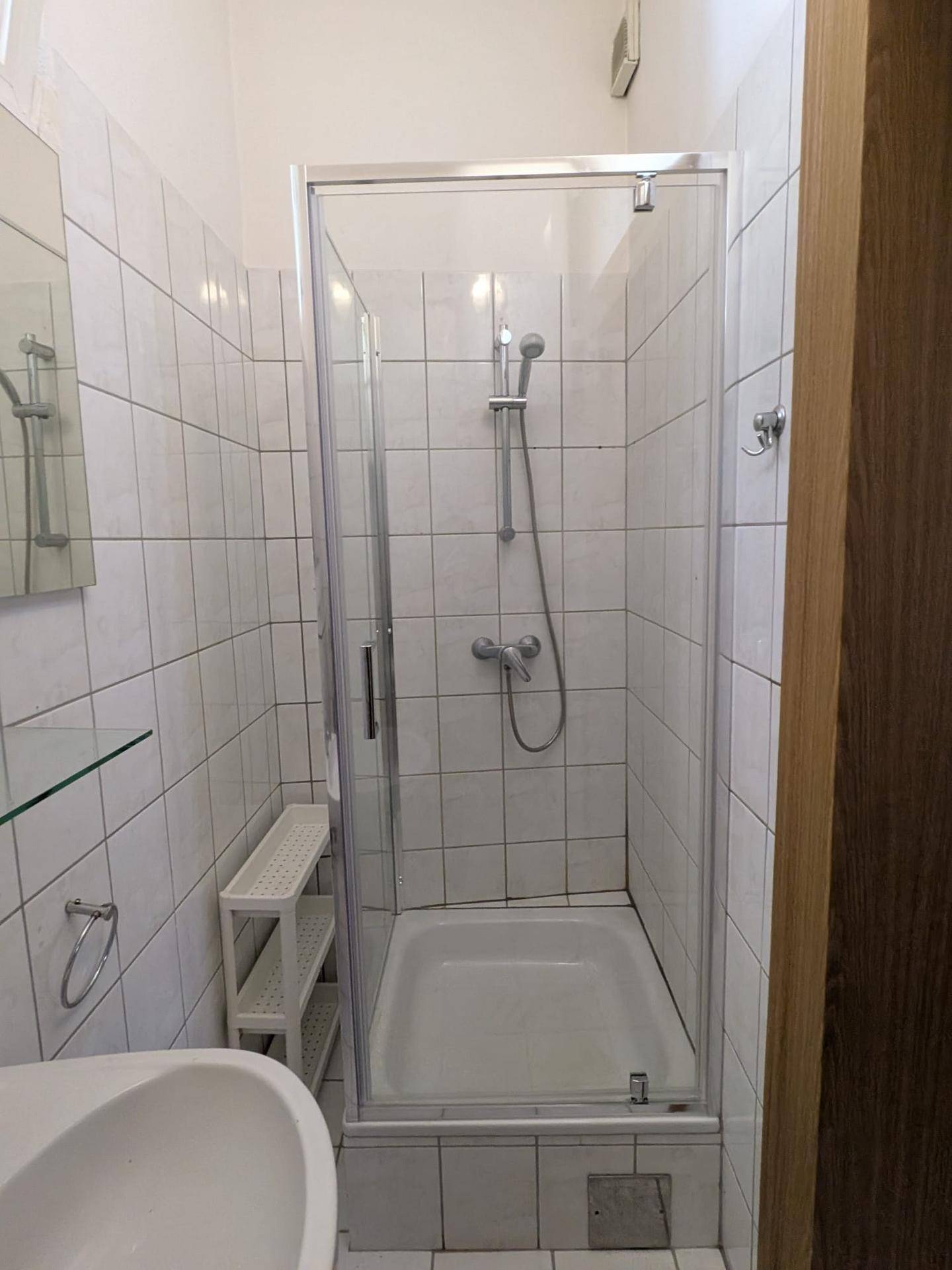Praktisches Badezimmer mit weißen Fliesen und einer Duschkabine, die eine effiziente Raumnutzung ermöglicht.