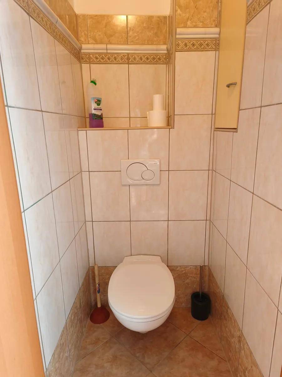 Separates WC mit wandhängender Toilette und hellen Fliesen an Wänden und Boden.