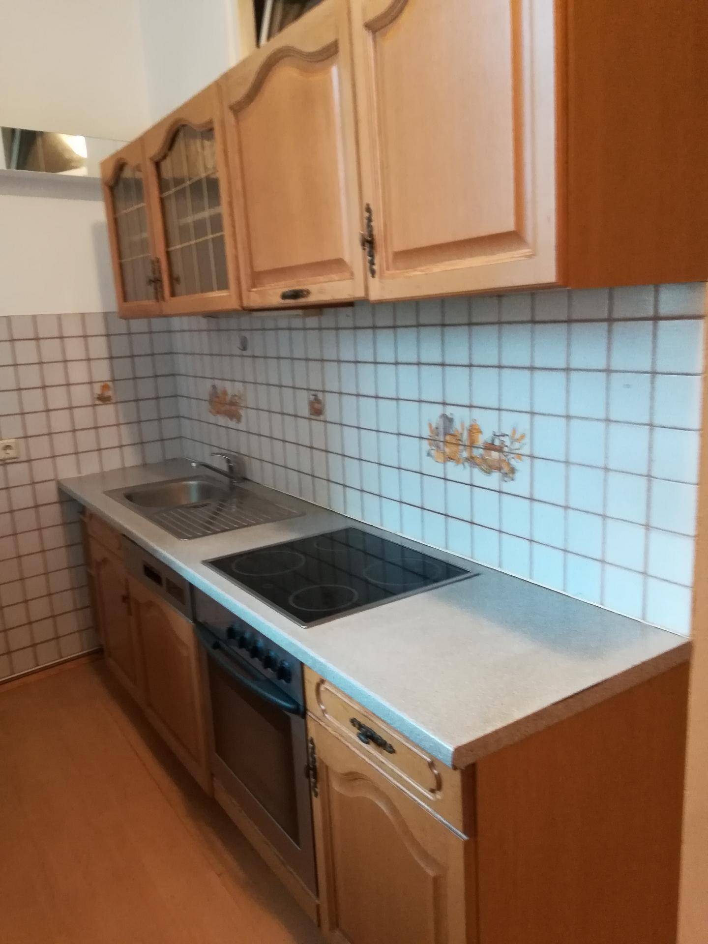 Funktionale Küche mit traditionellen Holzschränken, gefliestem Spritzschutz und integriertem Kochfeld.