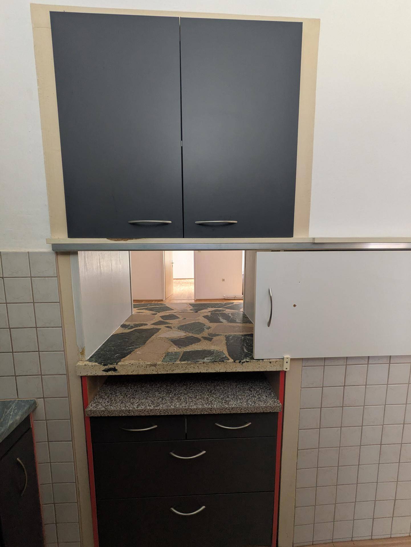 Teilweise eingerichtete Küche mit dunklen Oberschränken und gefliestem Bereich, Blick in einen weiteren Raum.