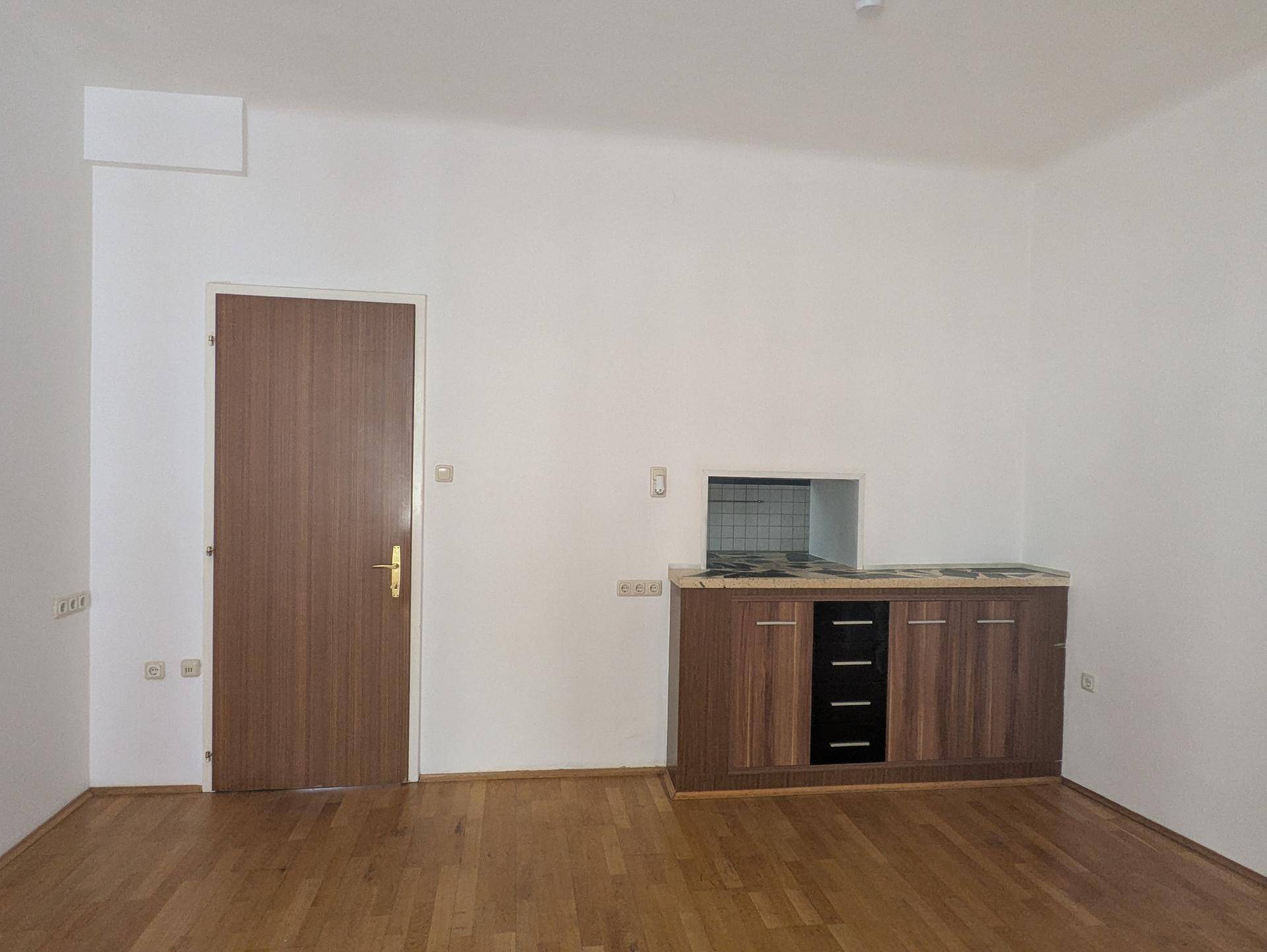 Heller Raum mit Holzboden und einer kleinen Küchenzeile, bereit für die individuelle Gestaltung.