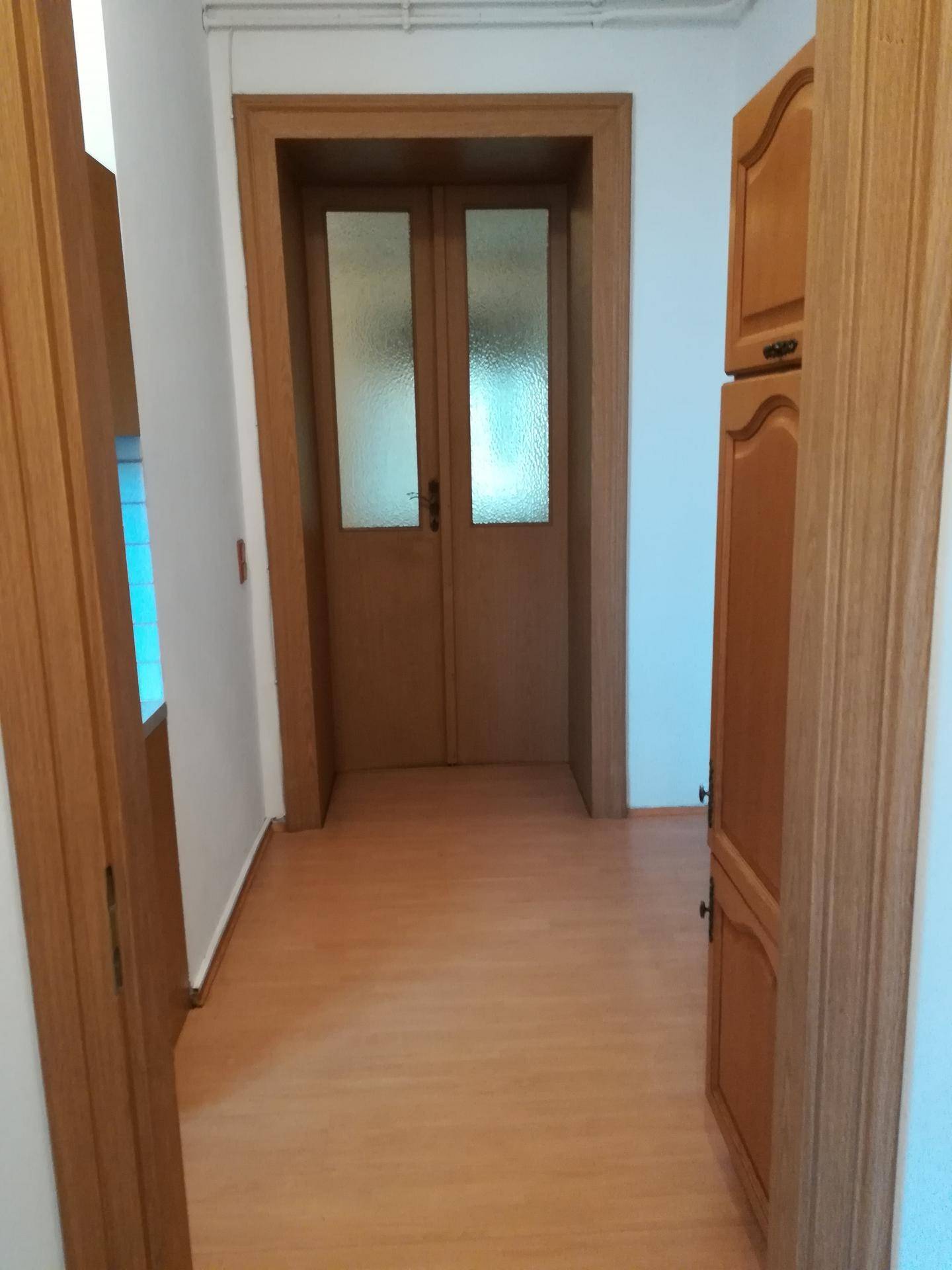 Flur mit hellem Laminatboden und Holztüren, der zu weiteren Räumen der Wohnung führt.