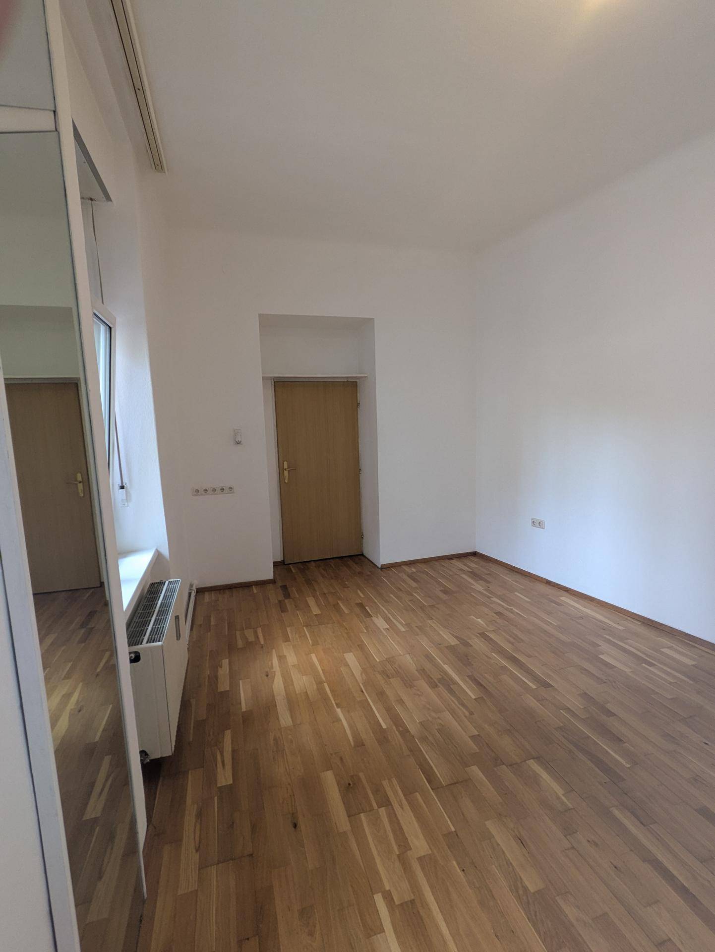 Heller Wohnraum mit klassischem Parkettboden und einer Tür, die zu einem weiteren Zimmer führt.