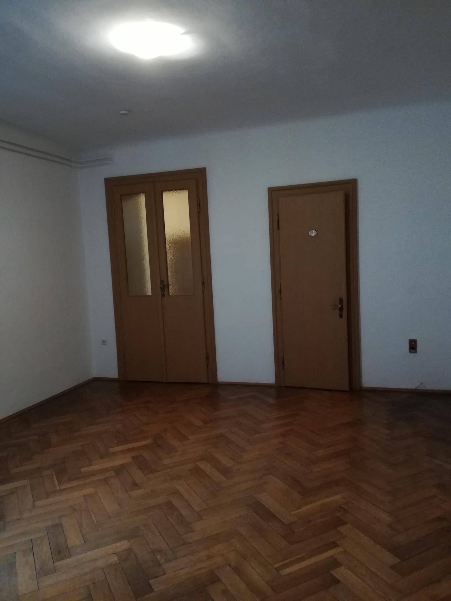 Geräumiges Zimmer mit elegantem Fischgrätparkett und zwei Holztüren, das eine klassische Atmosphäre schafft.
