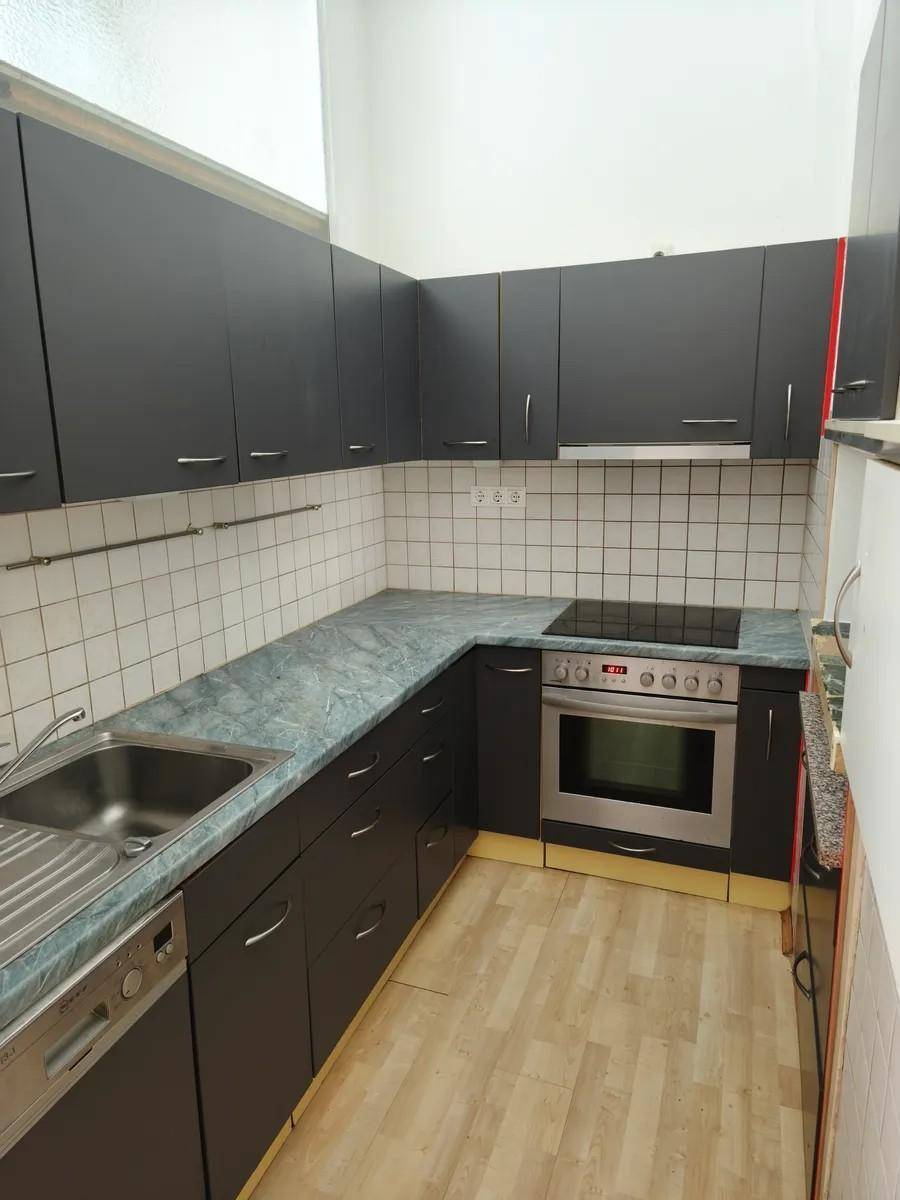 Kleine Küche mit dunklen Schränken, hellem Laminatboden und integrierten Geräten.
