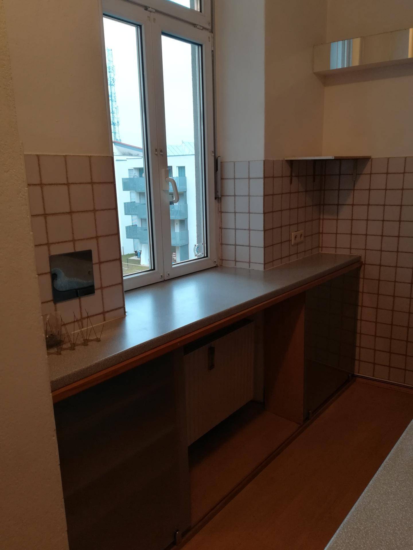 Küchenbereich mit Fenster, gefliestem Spritzschutz und Arbeitsplatte, bereit für die Installation weiterer Möbel.
