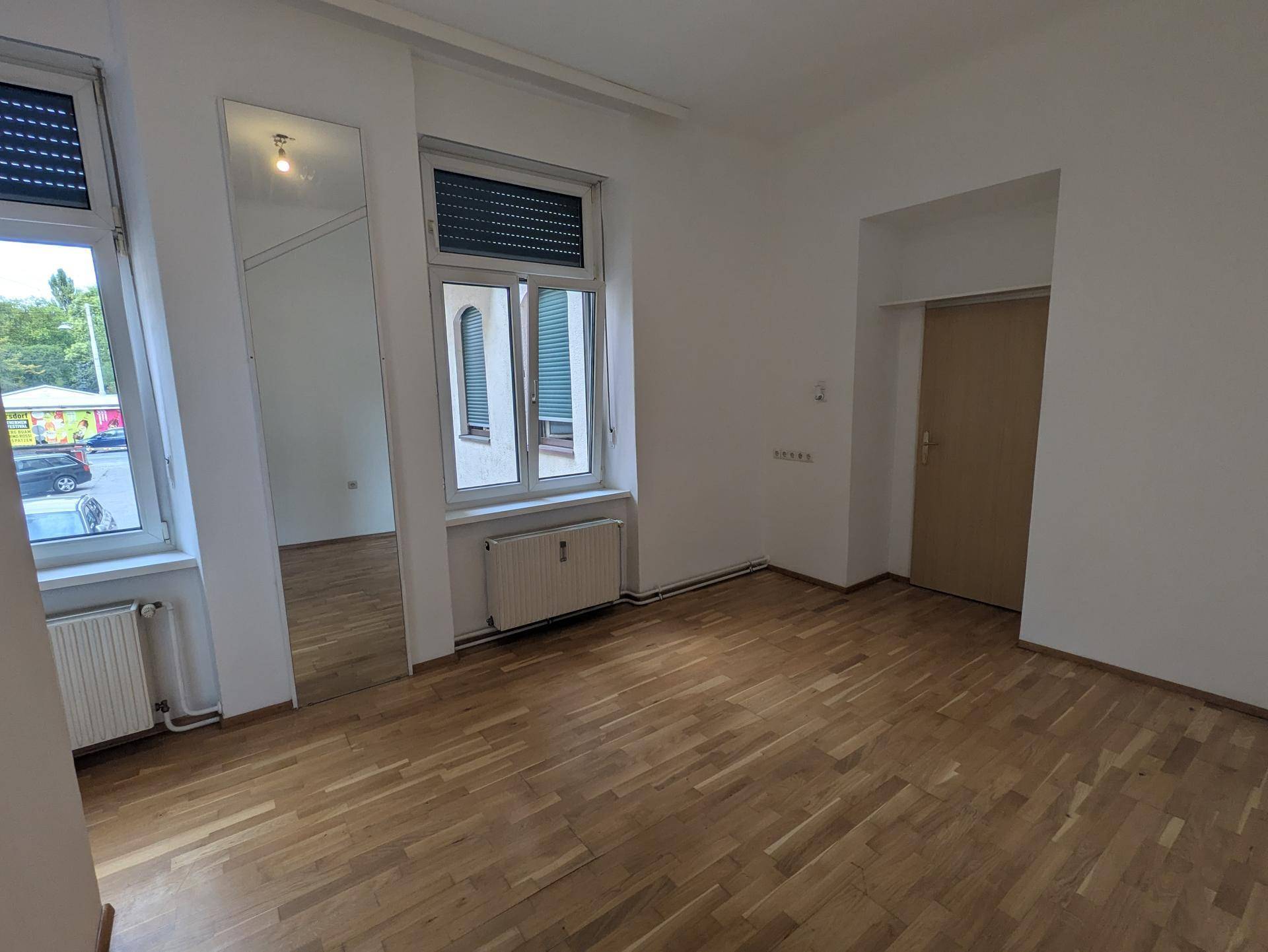 Helles Wohnzimmer mit Parkettboden und großen Fenstern, die einen Blick auf die Straße bieten.