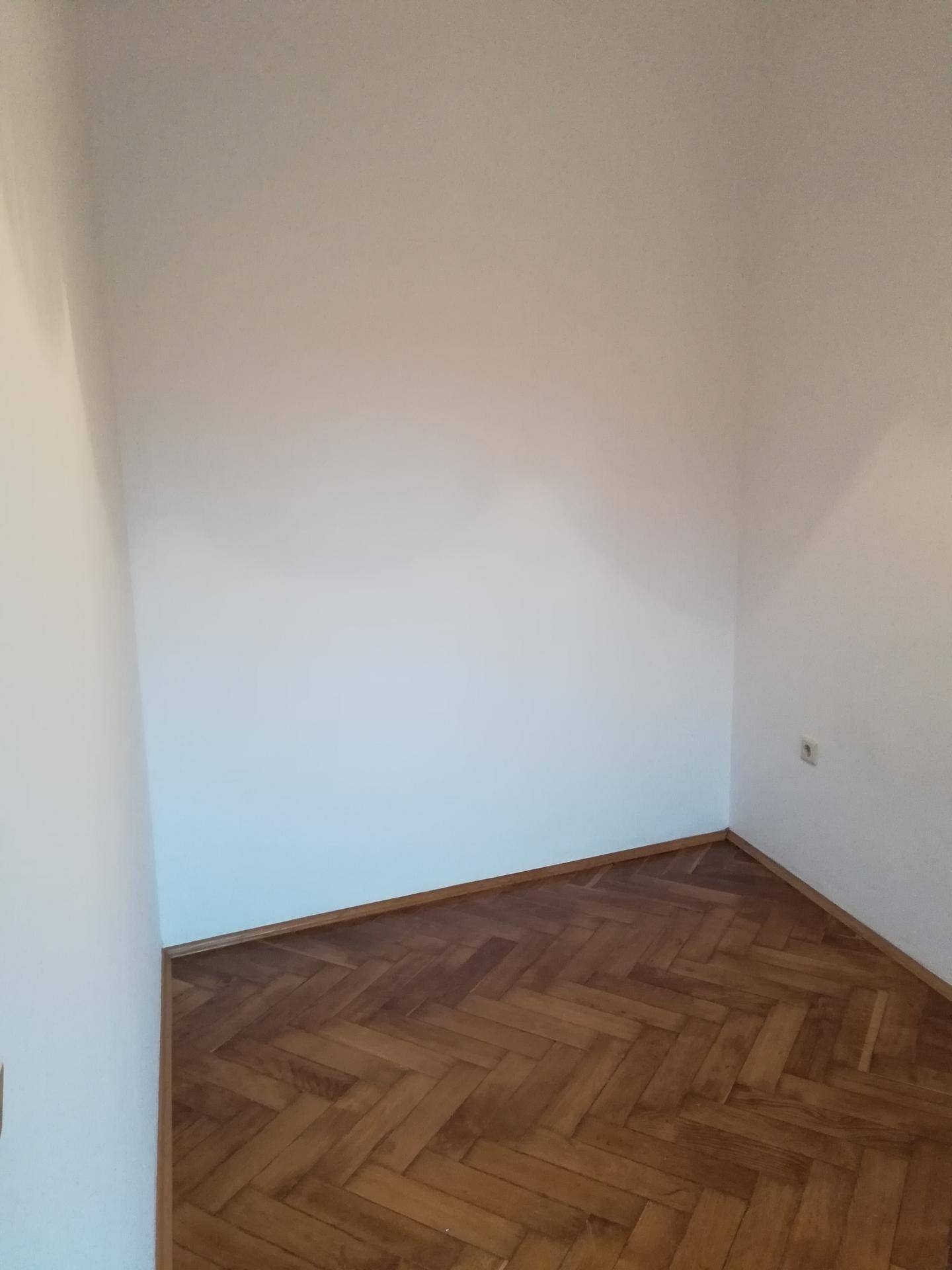 Leere Ecke eines Zimmers mit klassischem Fischgrätparkett, das eine warme und einladende Atmosphäre schafft.